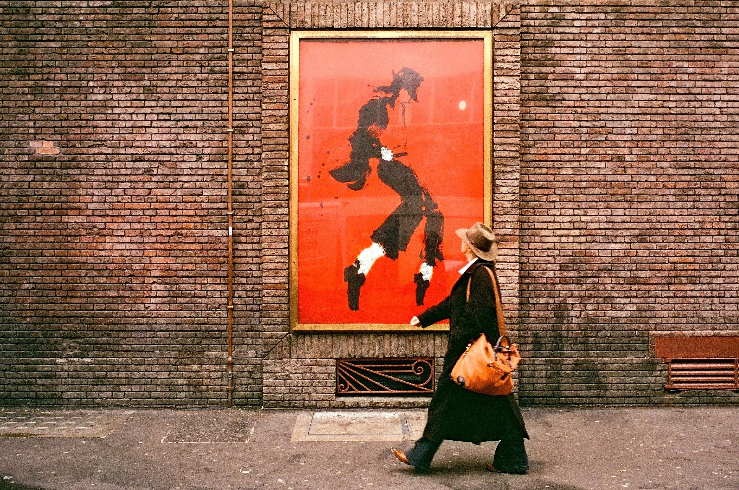 A person walking past a red and black abstract portrait on a brick wall.