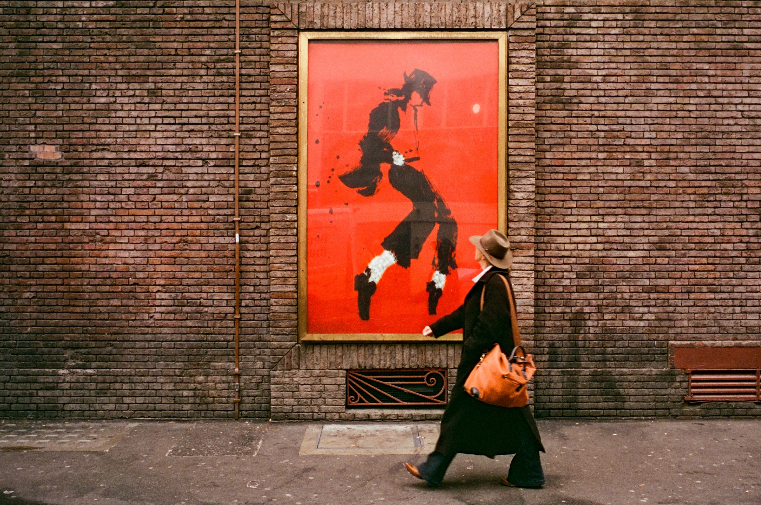 A person walking past a red and black abstract portrait on a brick wall.