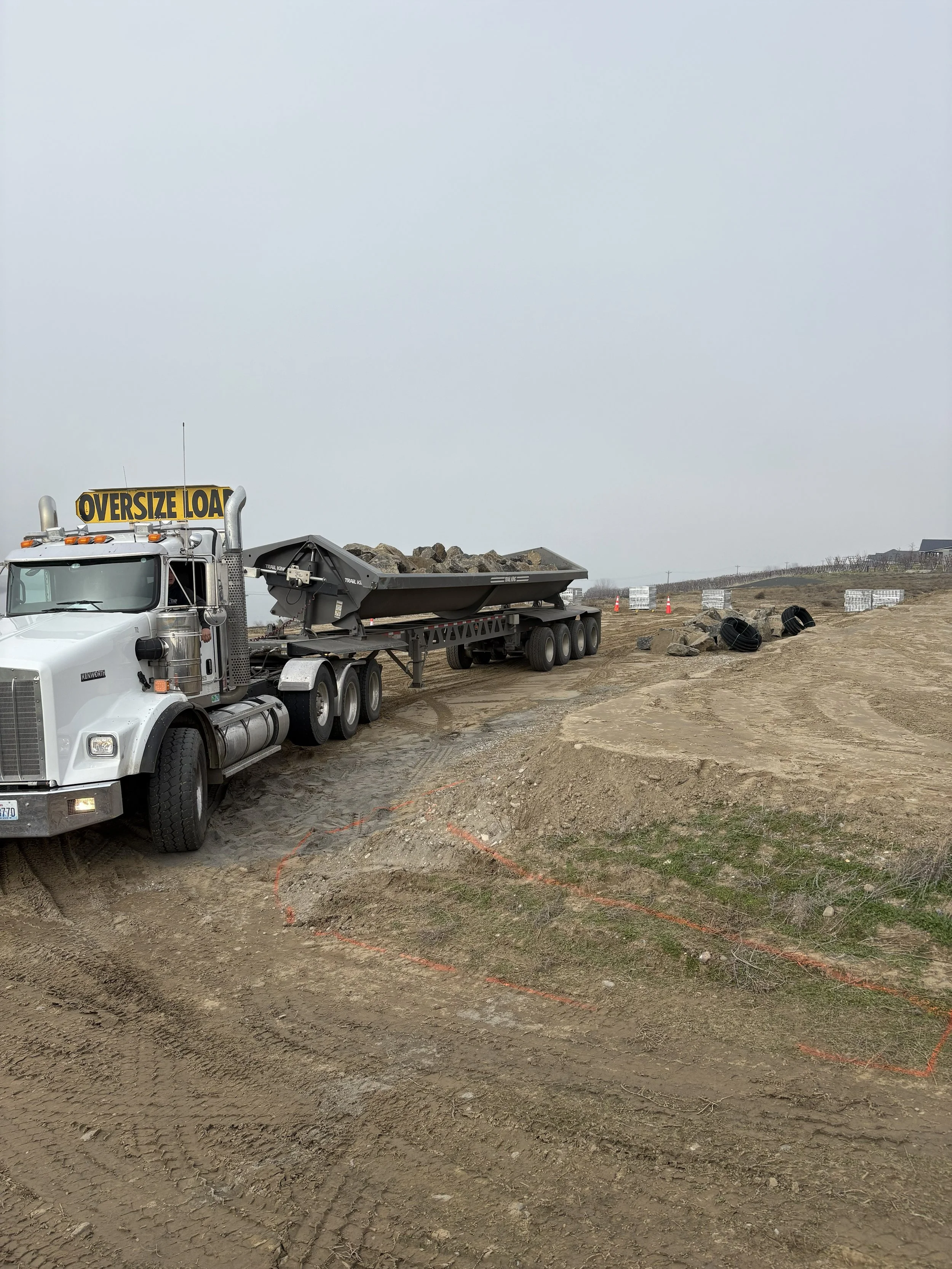 Construction site with a large dump truck and an uneven dirt ground, surrounded by construction markers and equipment.