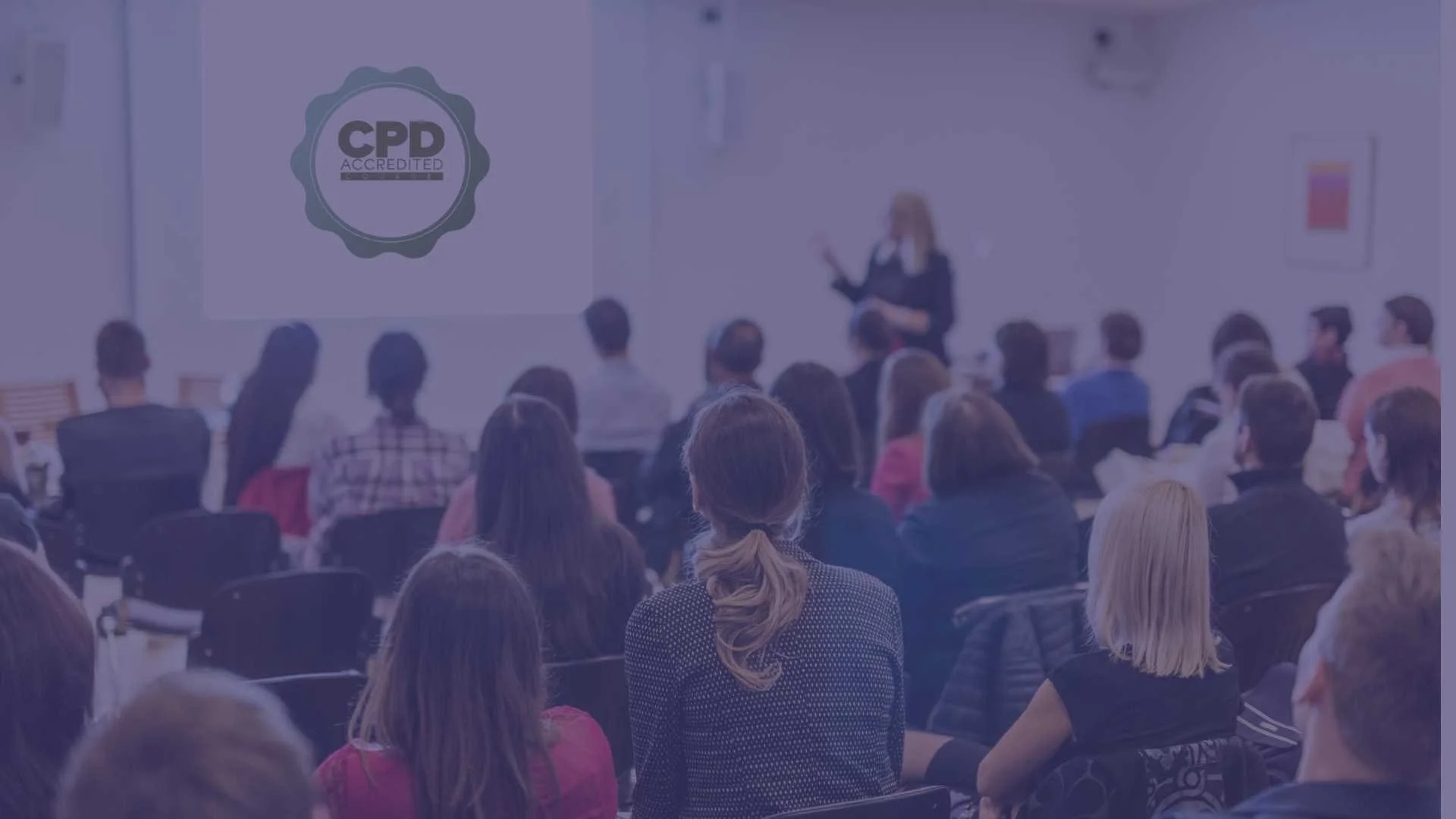 A woman giving a presentation in front of a seated audience in a conference room, with a CPD accredited badge displayed on a screen.