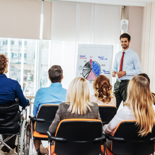 A man standing in front of a whiteboard giving a presentation to a group of seated adults in a conference room.