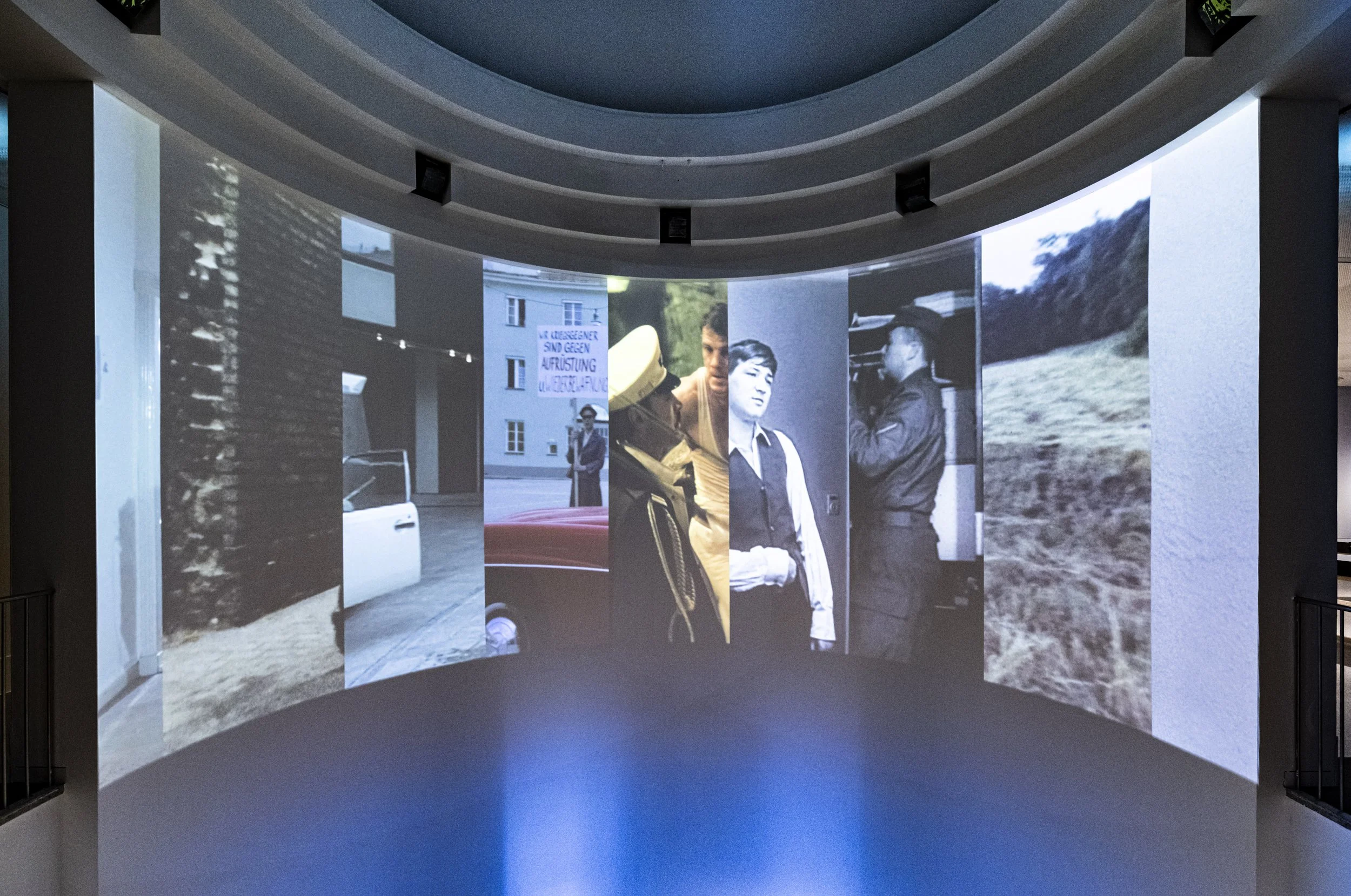 Mehrere vertikale Bildschirme mit Schwarzweiß- und Farbfotografien in einer kreisförmigen Anordnung.