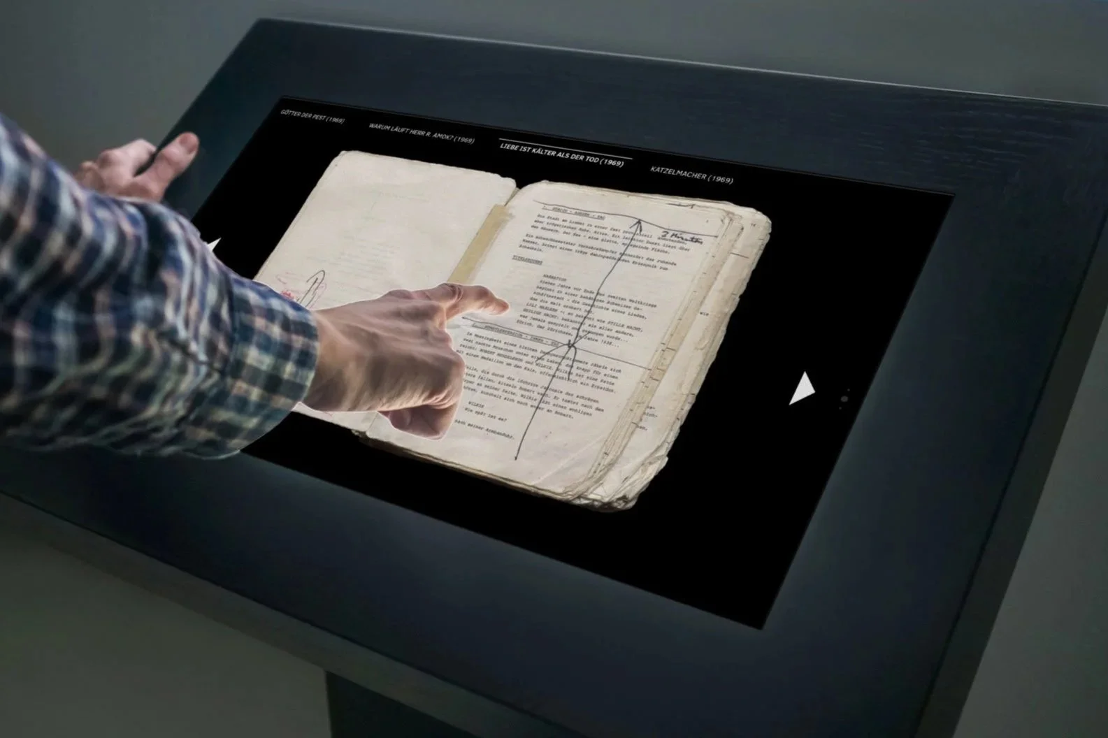 Hand blättert auf einem Touchscreen durch ein eingescanntes Drehbuch – interaktive Medienstation im Ausstellungsraum