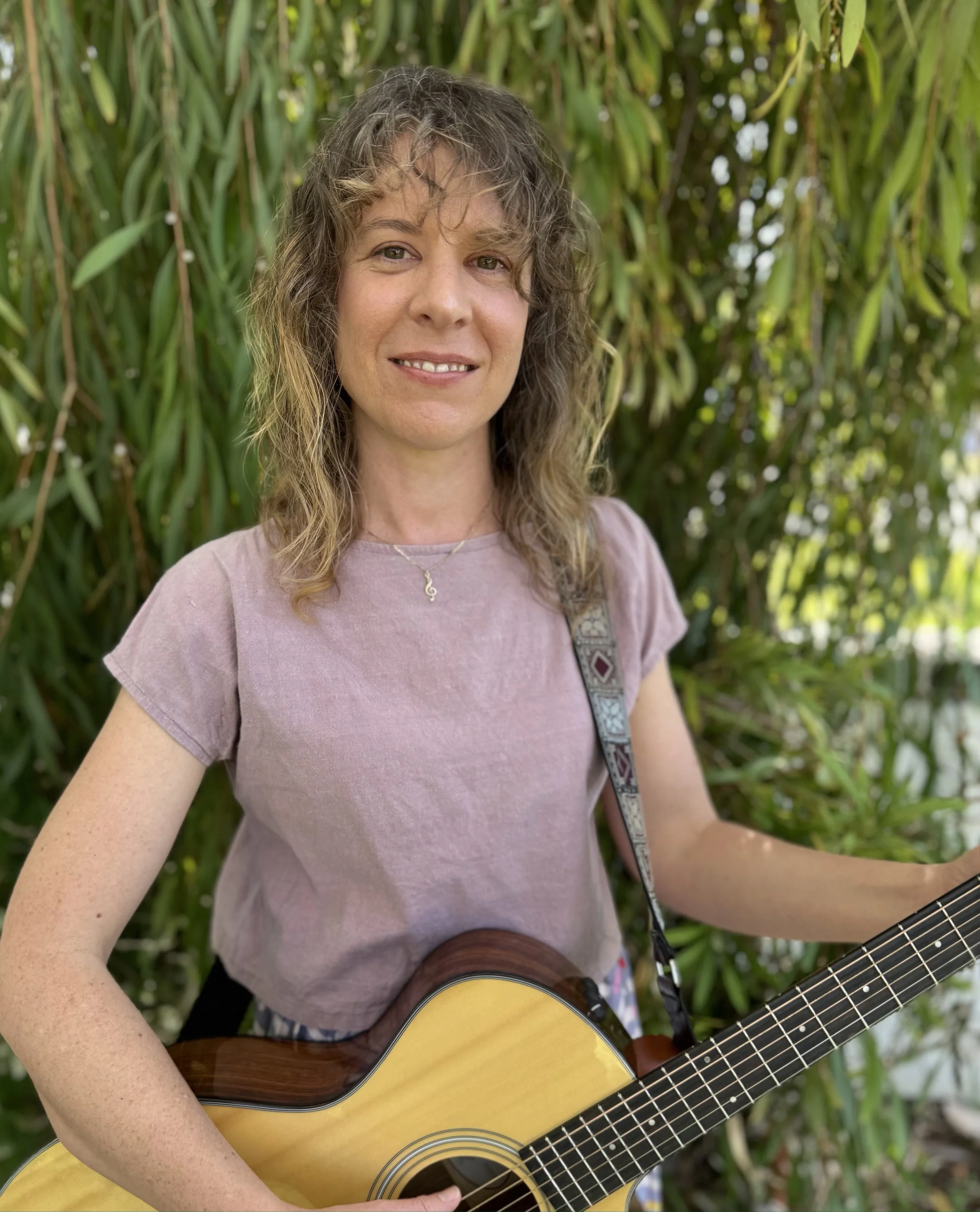 Photo of Anneke de Rooij music therapist holding a guitar and smiling