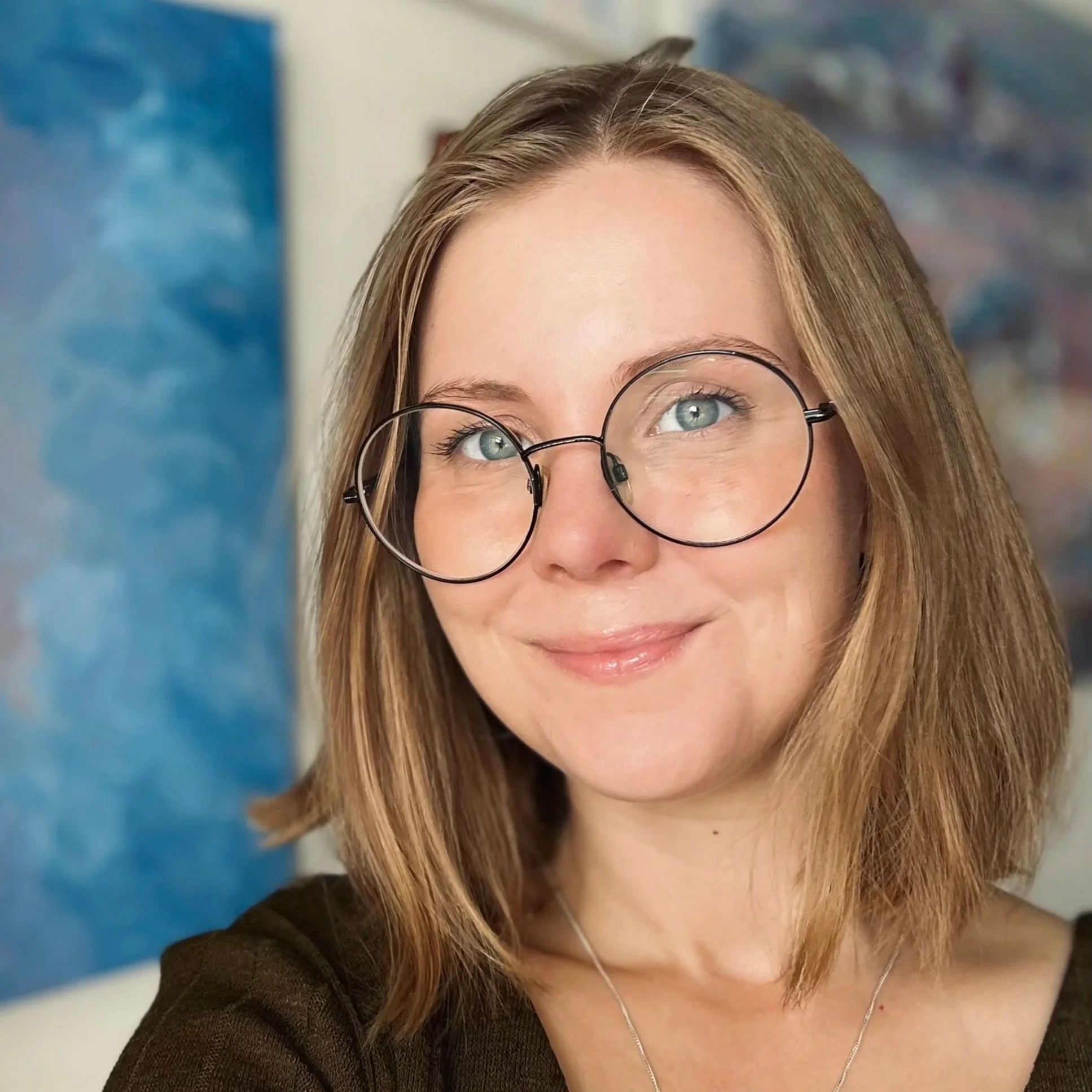 Porträtt av Emelie, hon har glasögon, ler och tittar in i kameran.