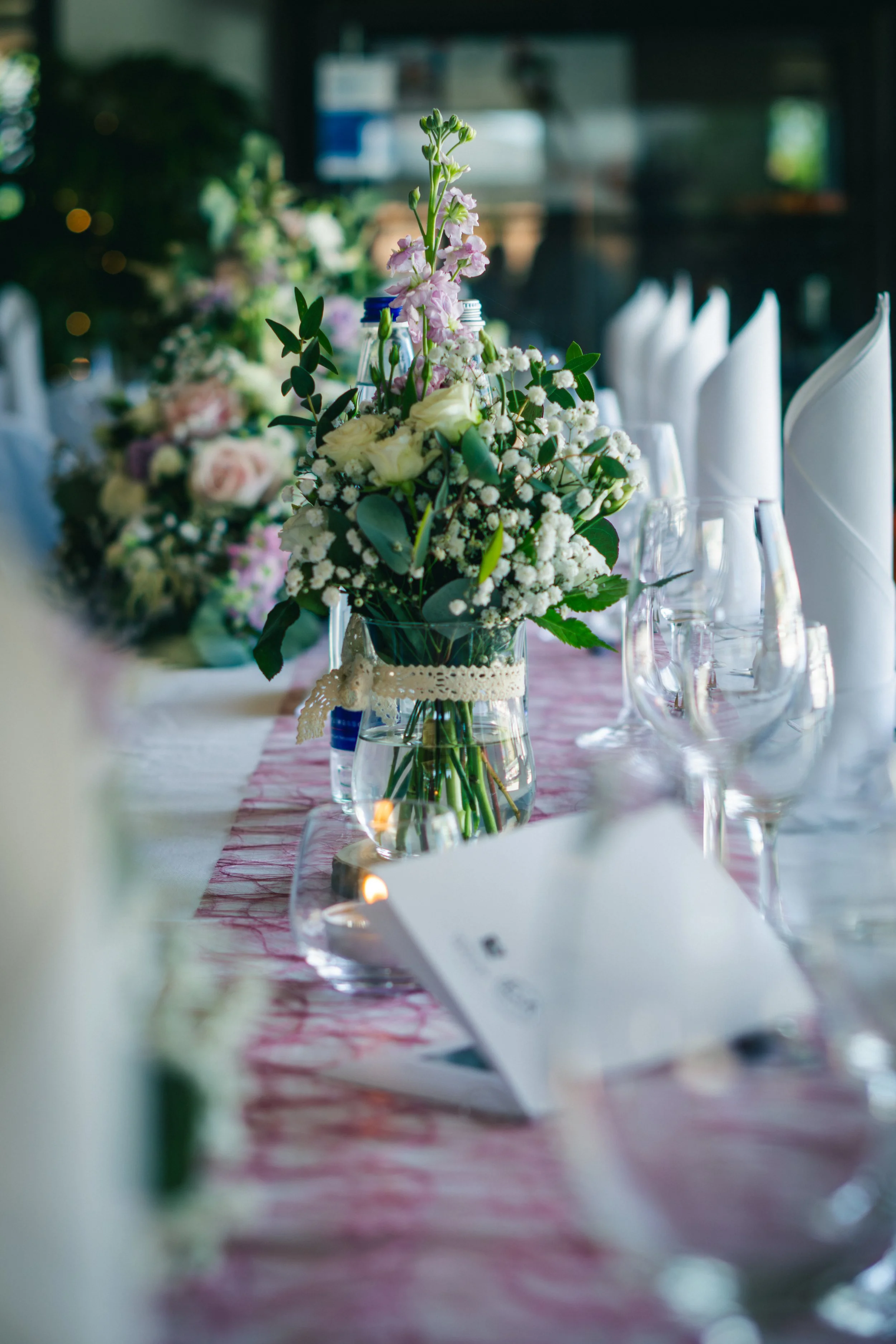 Blumenstrauß auf einem festlich gedeckten Tisch mit Gläsern, weißen Servietten und einer Menükarte im Hintergrund.