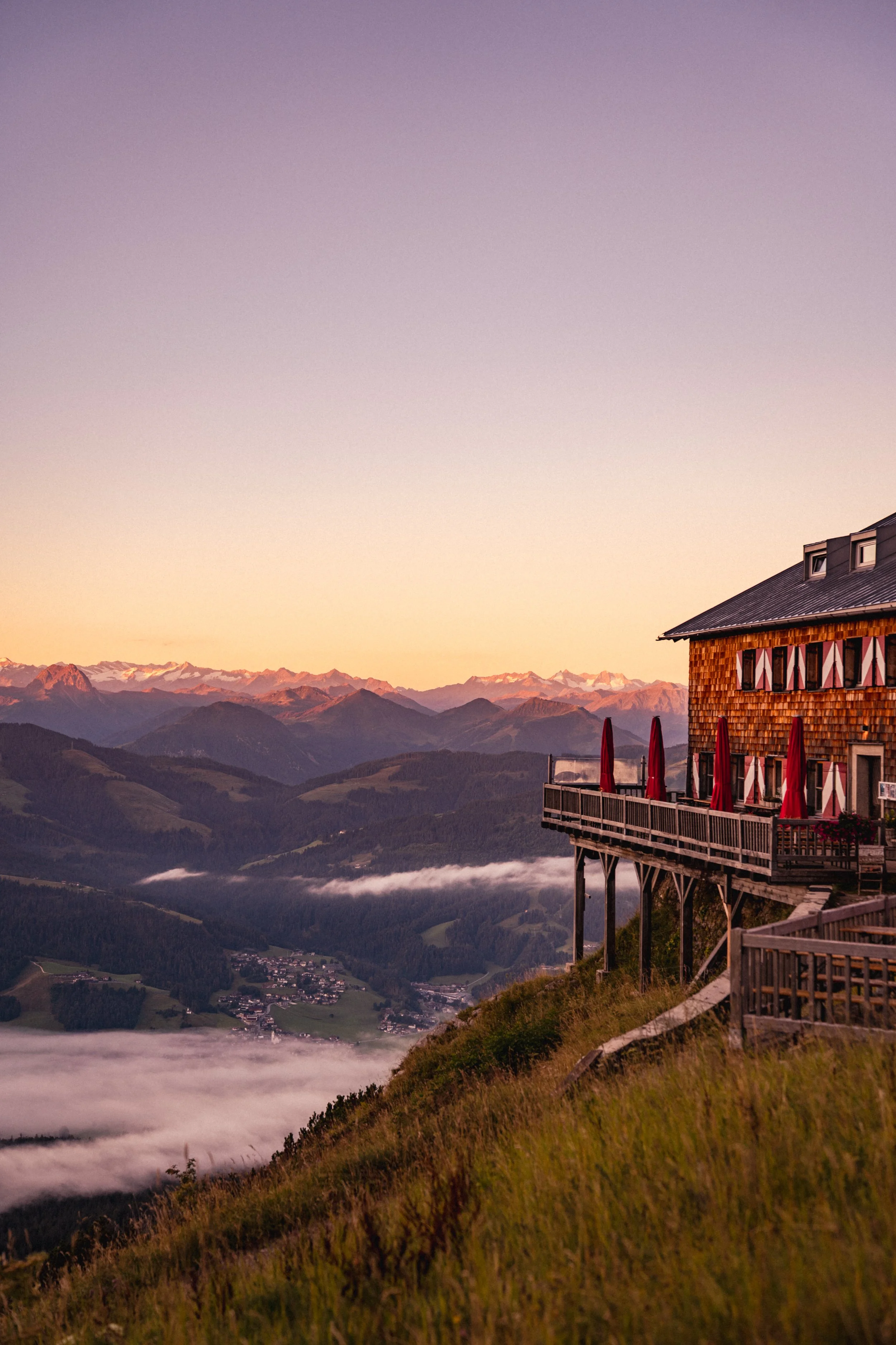 Ein Berghotel mit Balkon bei Sonnenaufgang, Blick auf Mountains und Nebel im Tal.