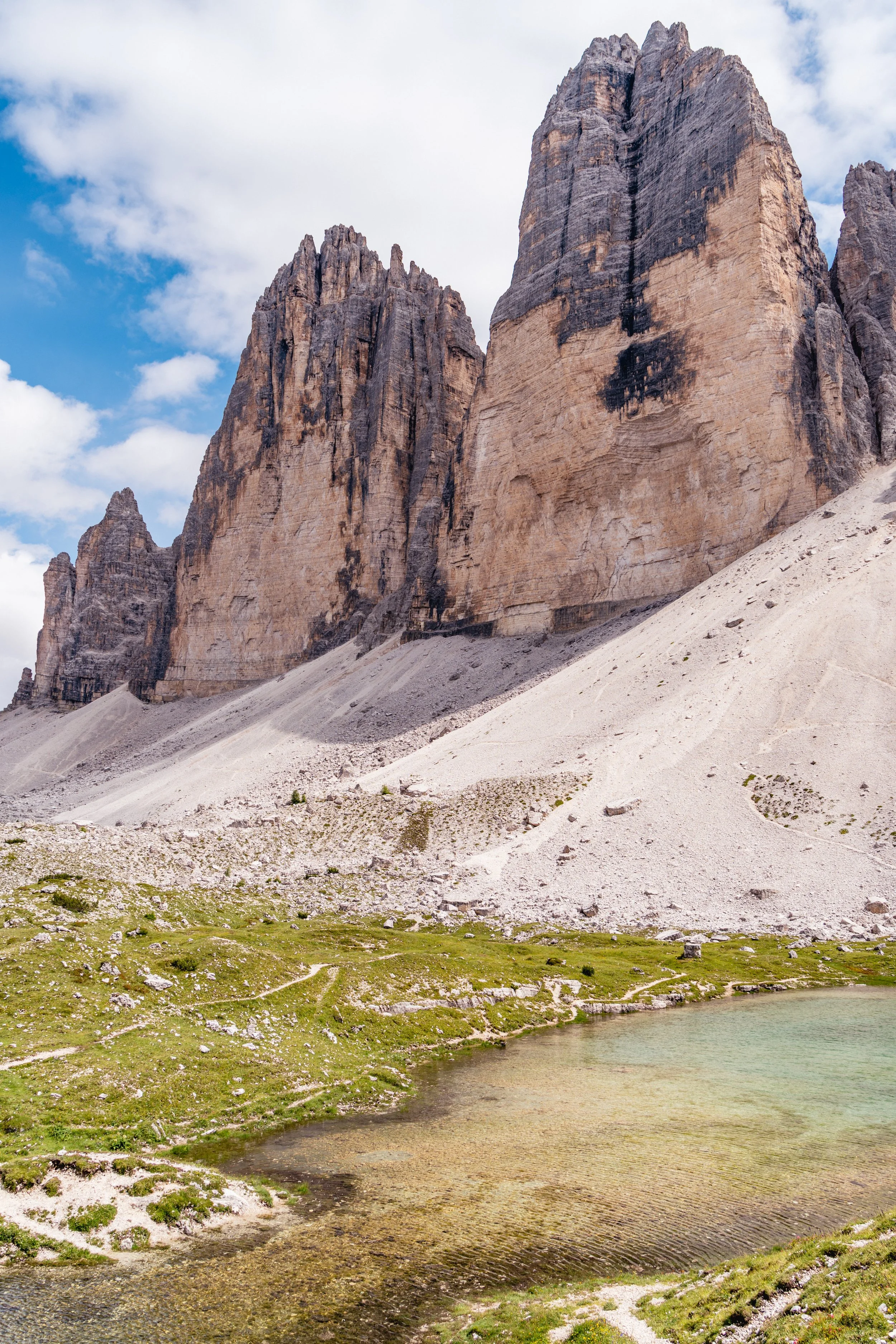 Berglandschaft mit hohen Felswänden, einem kleinen See im Vordergrund und einer bewölkten Himmel