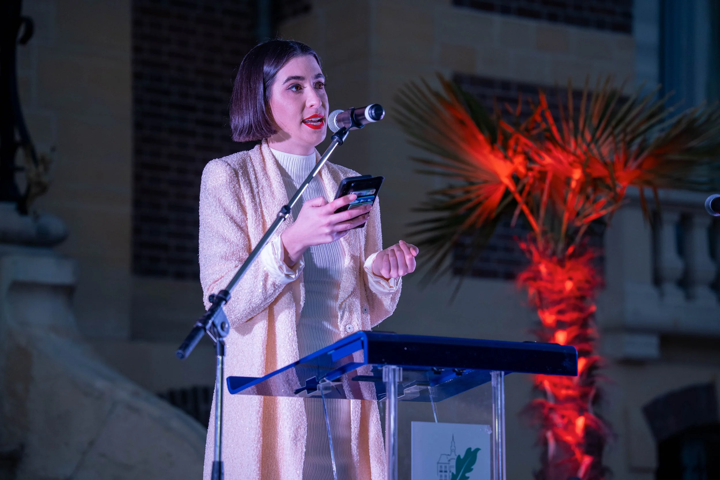 A modern backyard with a rectangular pool, three lounge chairs, surrounded by purple bushes, a large agave plant, and a house with a patio and trees in the background during sunset.