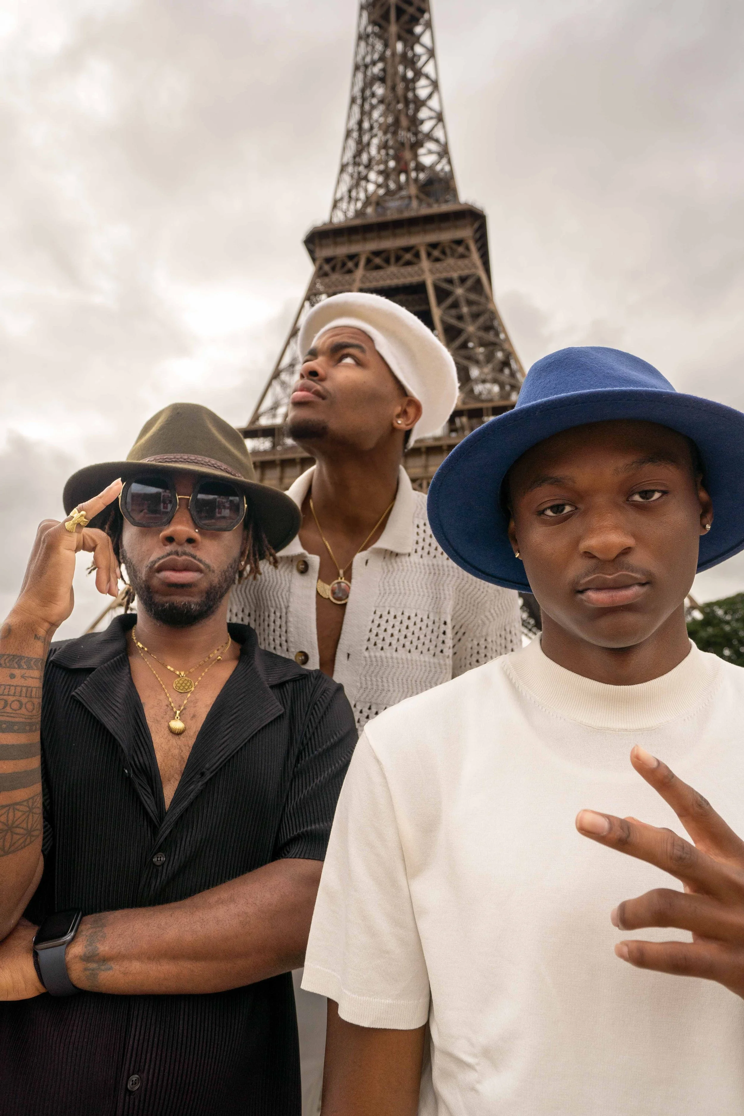 Three young men with fashionable clothing and accessories standing in front of the Eiffel Tower in Paris, France.