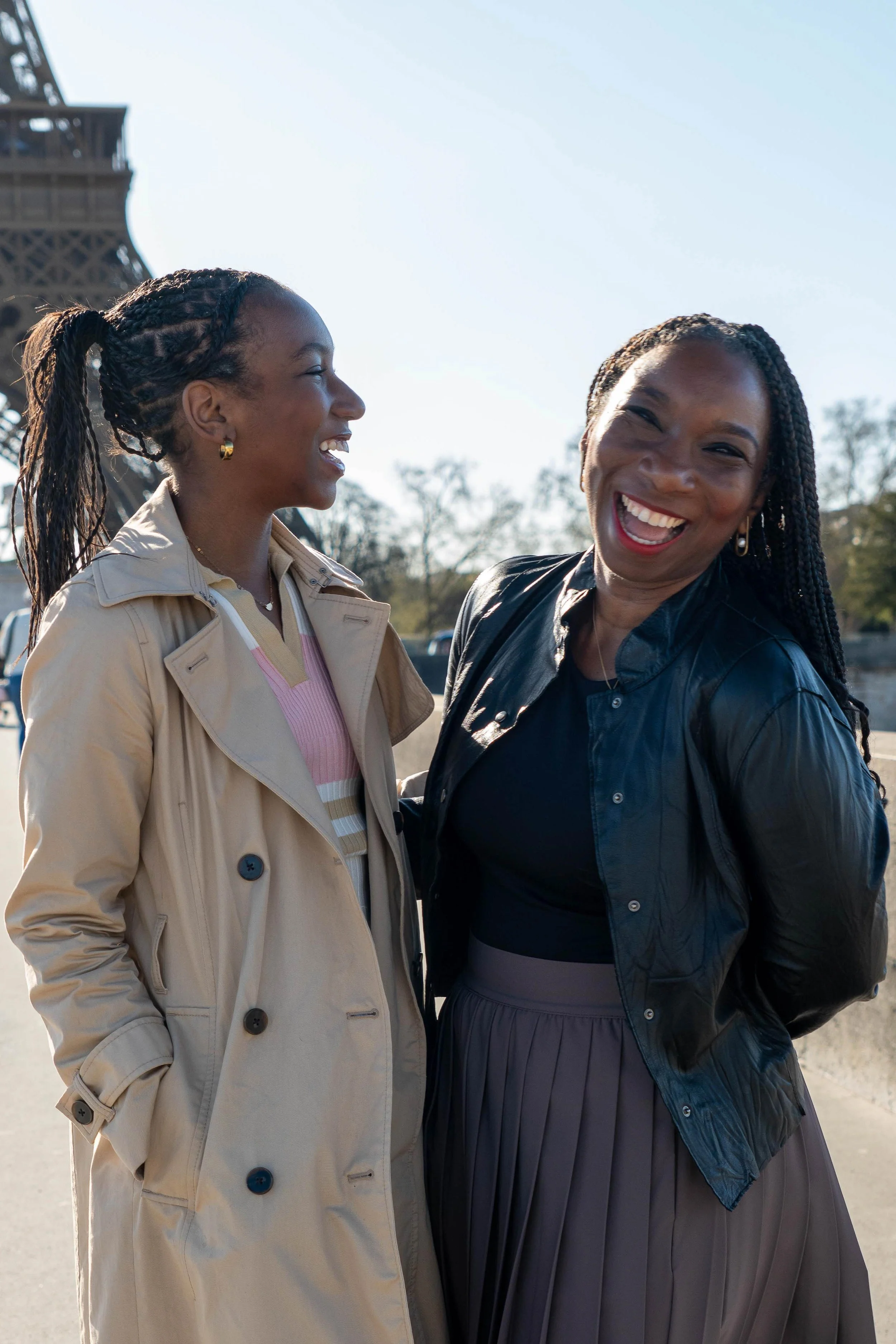Two women smiling and laughing outdoors with the Eiffel Tower in the background.