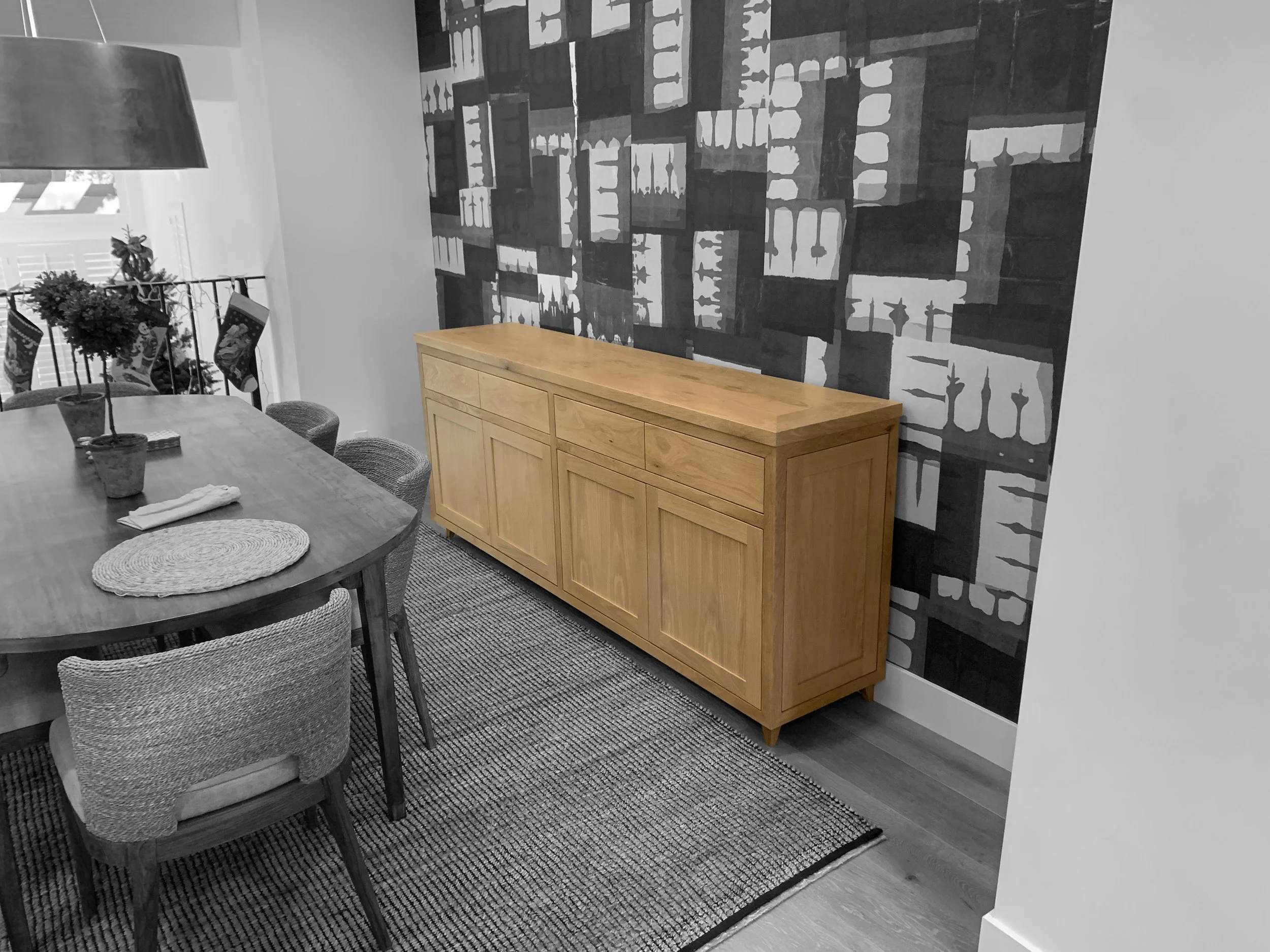 Une pièce de repas avec une table en bois, six chaises, un buffet en bois clair et un mur décoratif noir et blanc avec motif abstrait.