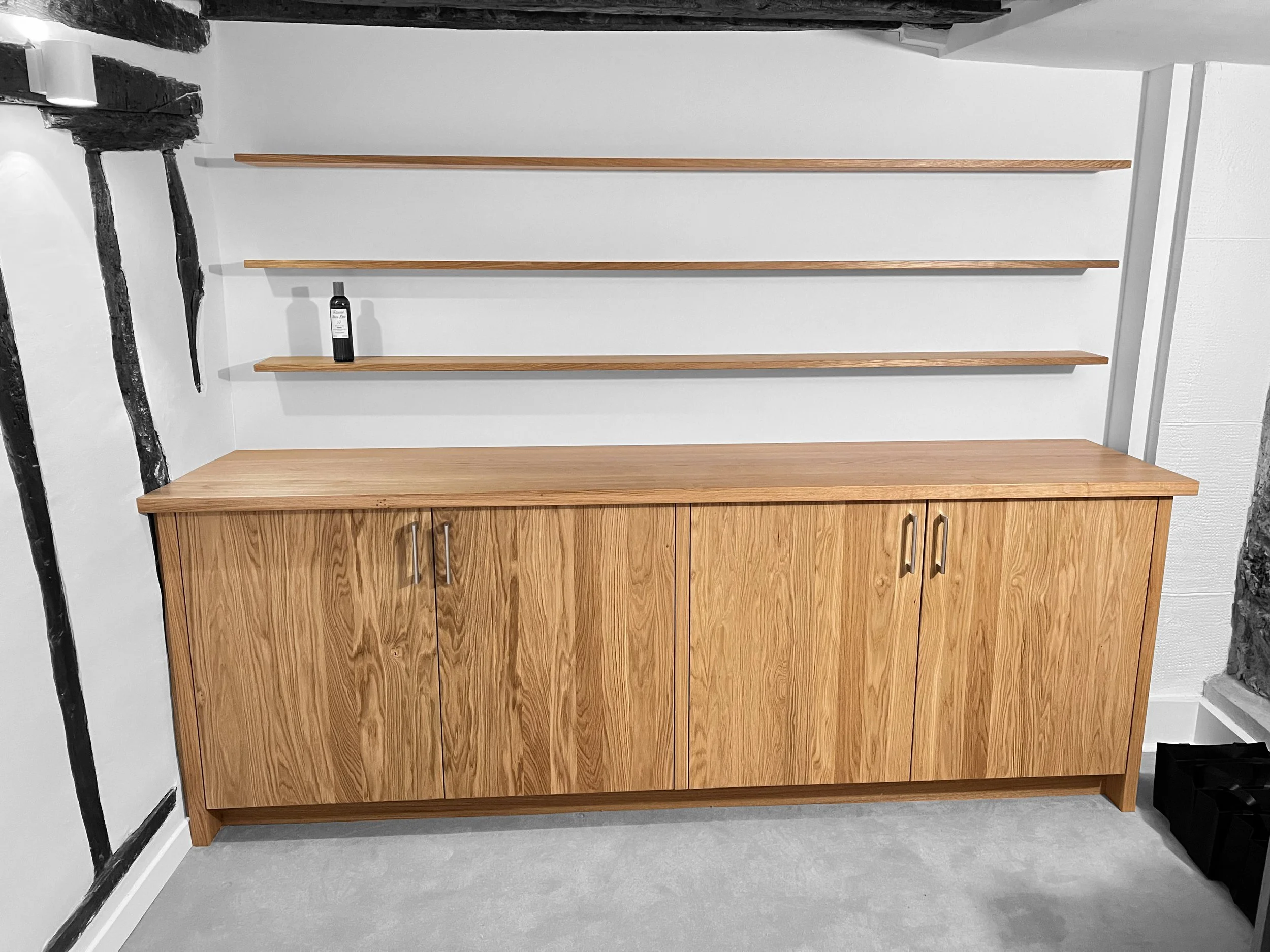 Mobil en bois avec portes, deux étagères en bois au mur avec une bouteille sur l'étagère supérieure.