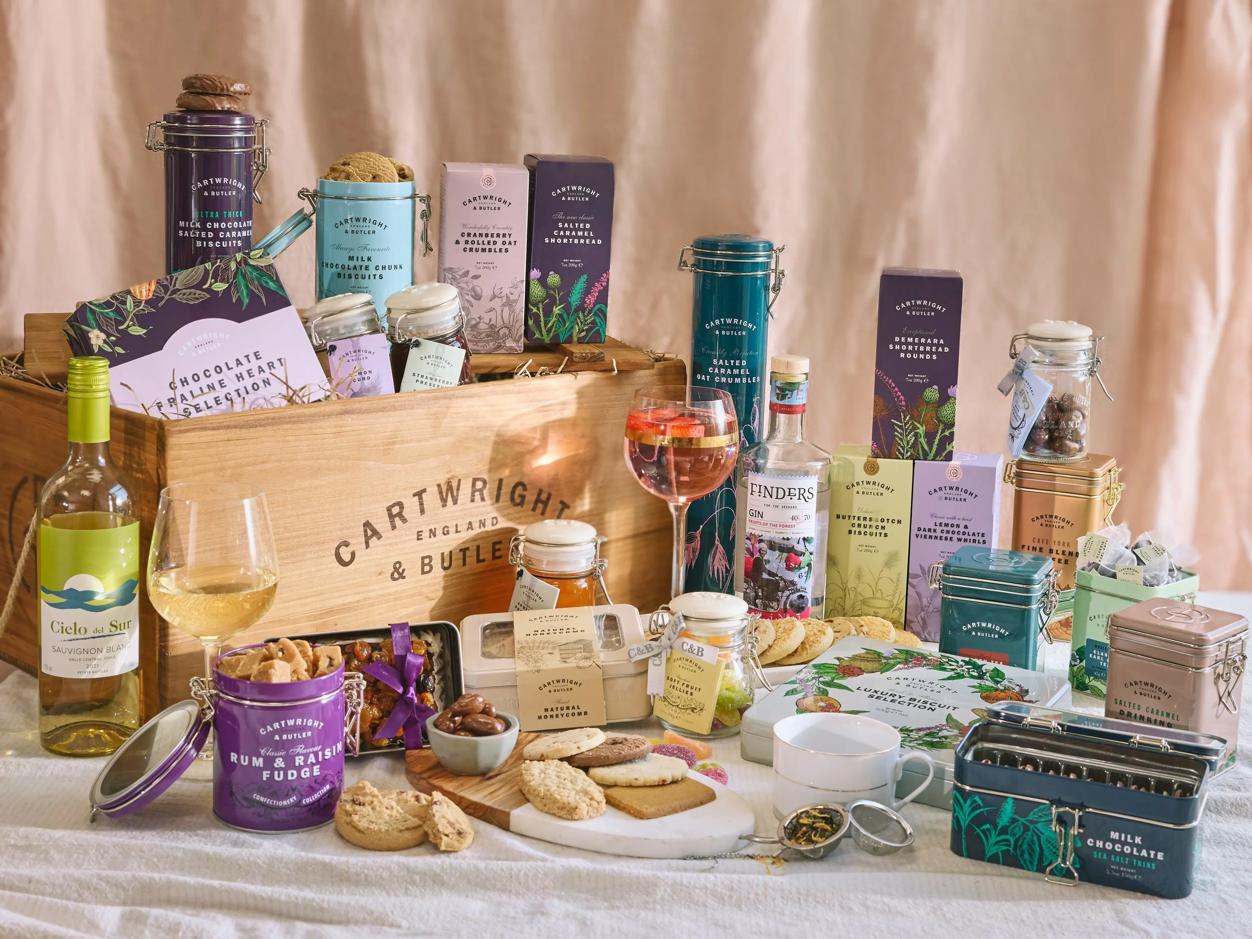 A display of assorted biscuits, chocolates, and beverages on a table with a wooden crate labeled 'Cartwright & Butler' in the background.