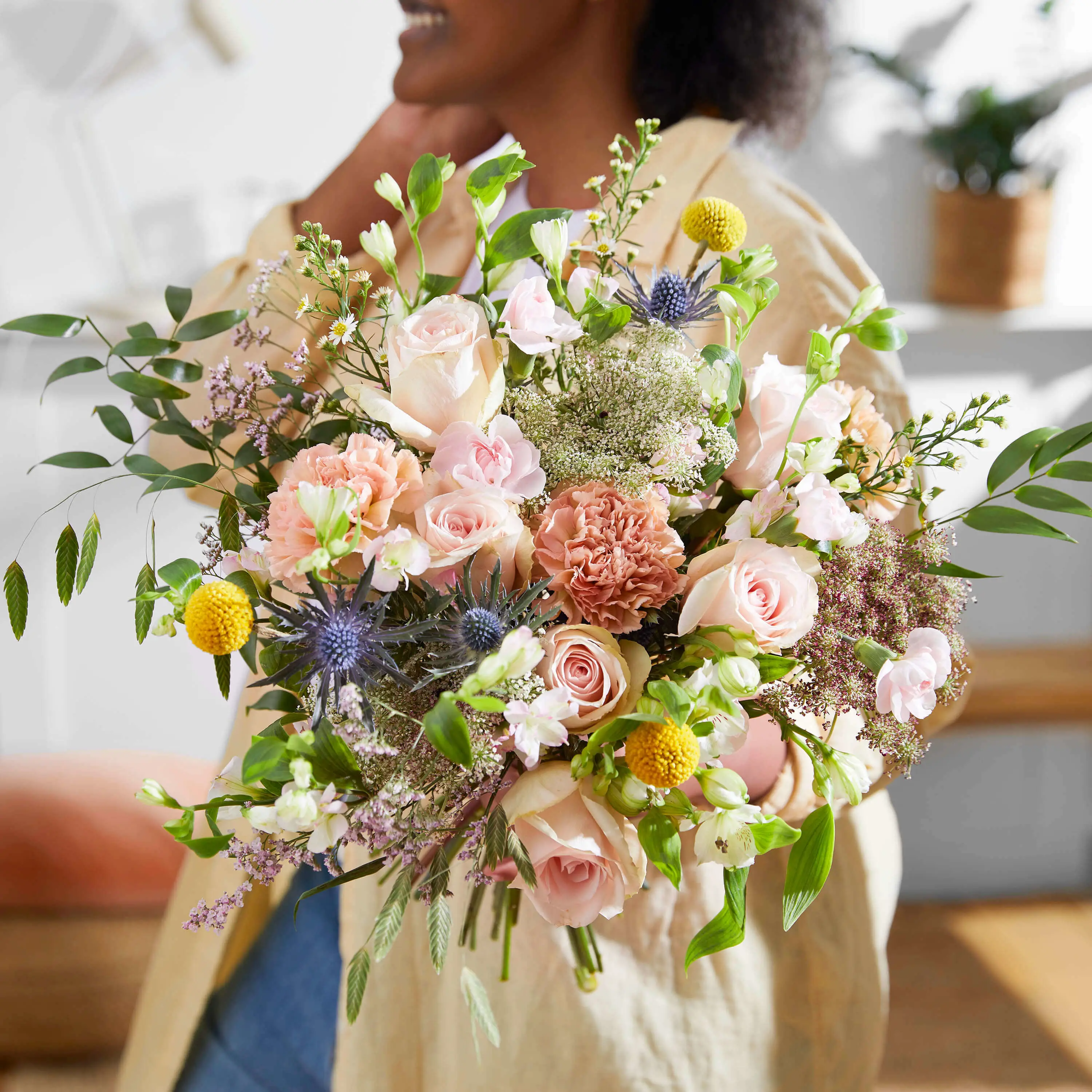Person holding a colorful bouquet of assorted flowers including roses, carnations, and greenery.