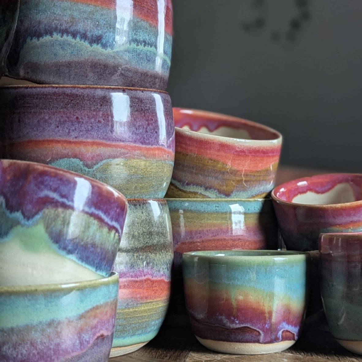 Bunte, handgefertigte Keramikschalen mit bunten, wellenartigen Mustern, stapelweise auf einem Holzoberfläche