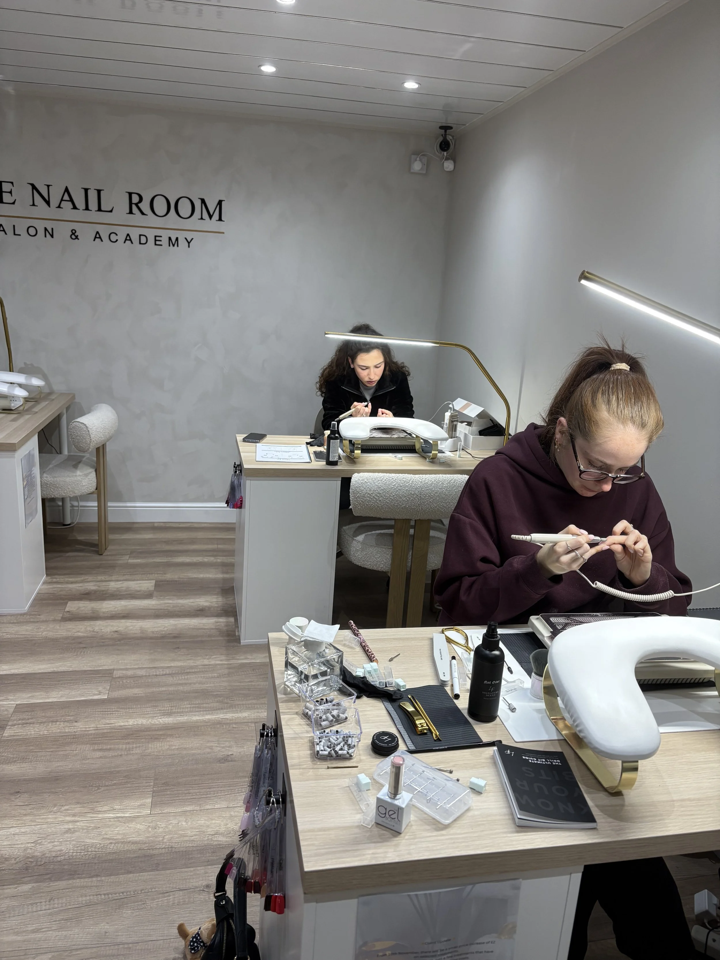 Nail salon with two women training on nail care at separate workstations at the nail room training academy