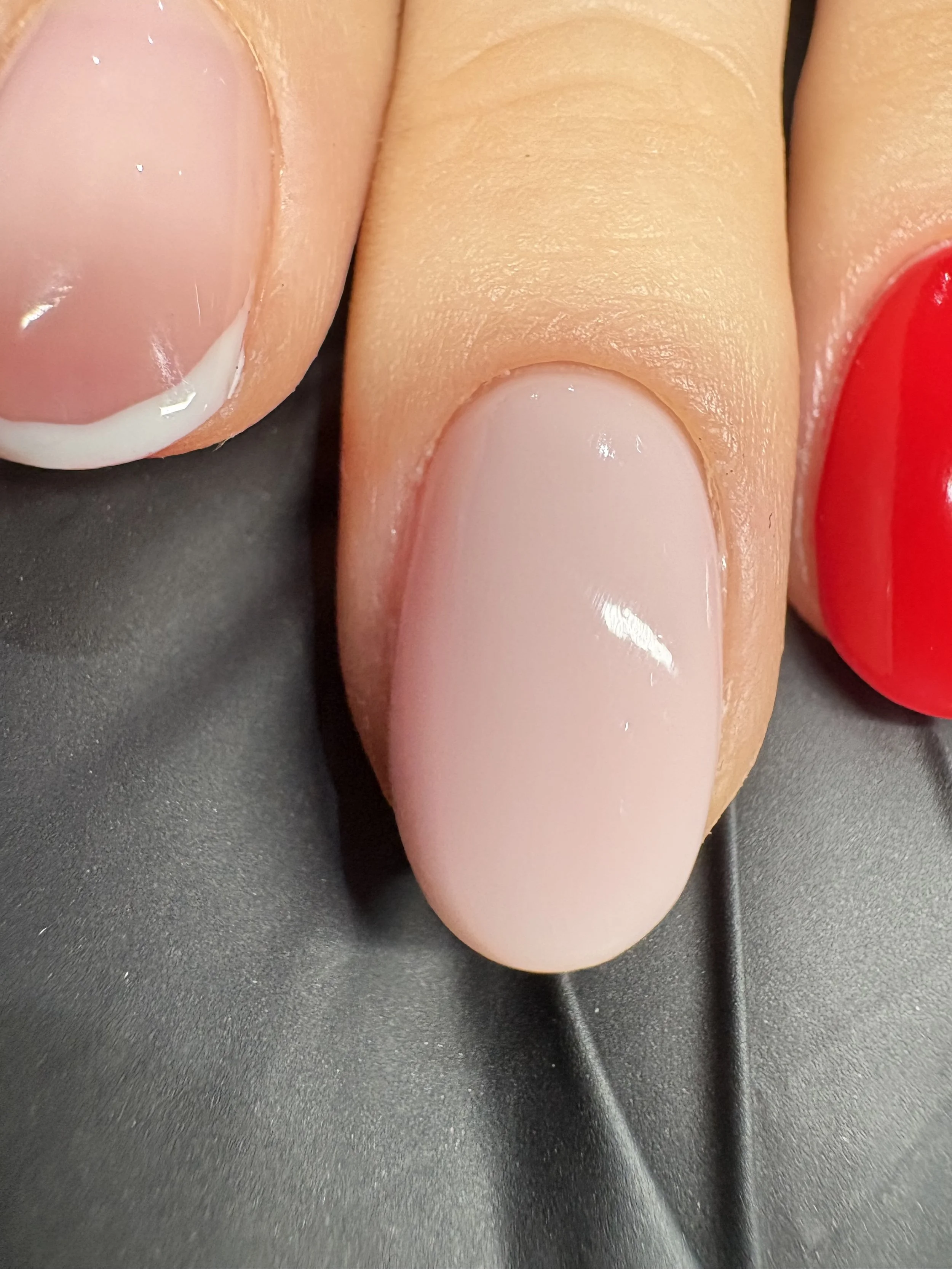 Close-up image of three fingers with manicured nails, the middle and left nails with a natural light pink polish, and the right nail painted with bright red polish.
