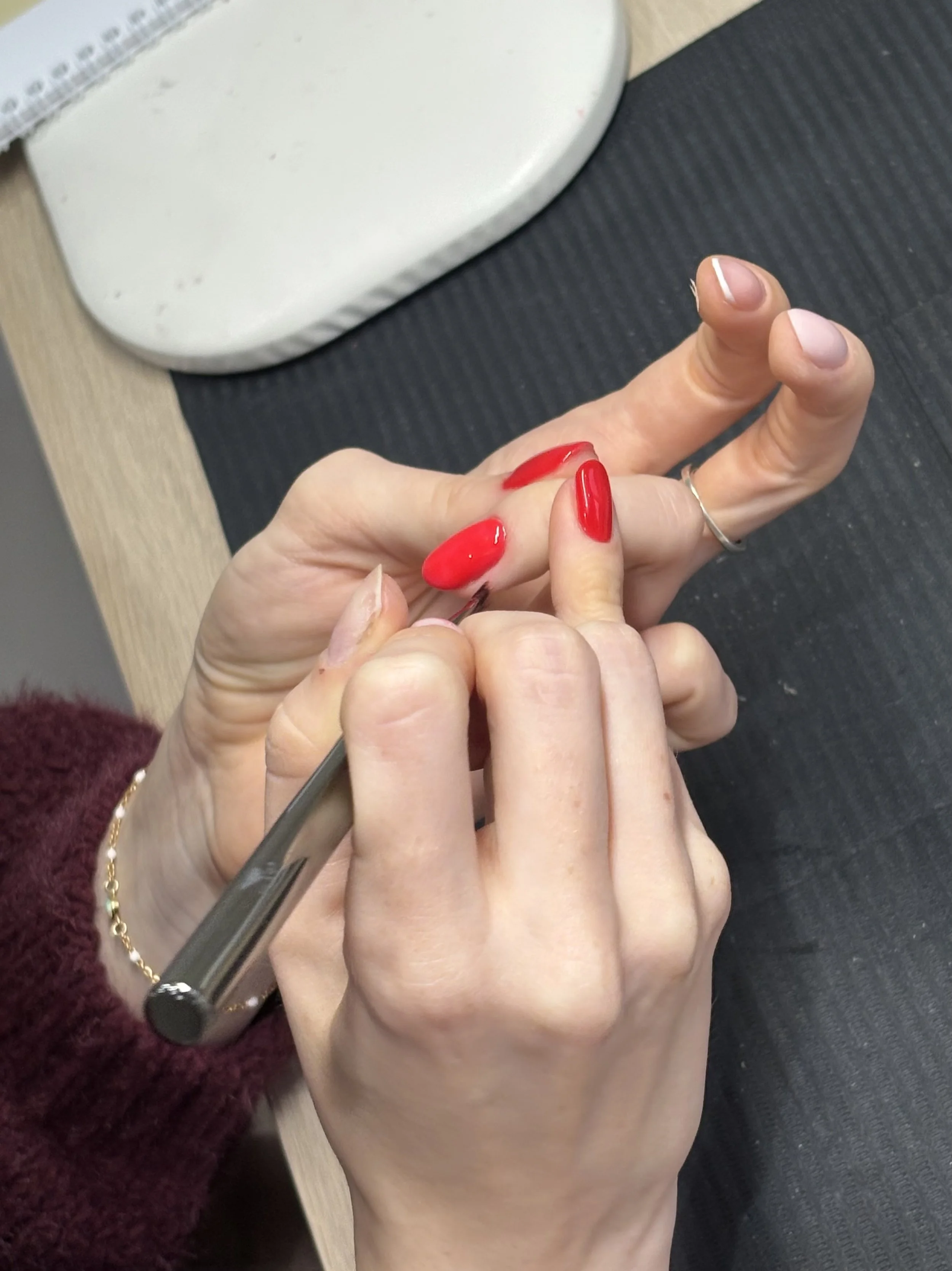 Person learning manicure with red nail polish at a nail salon table.