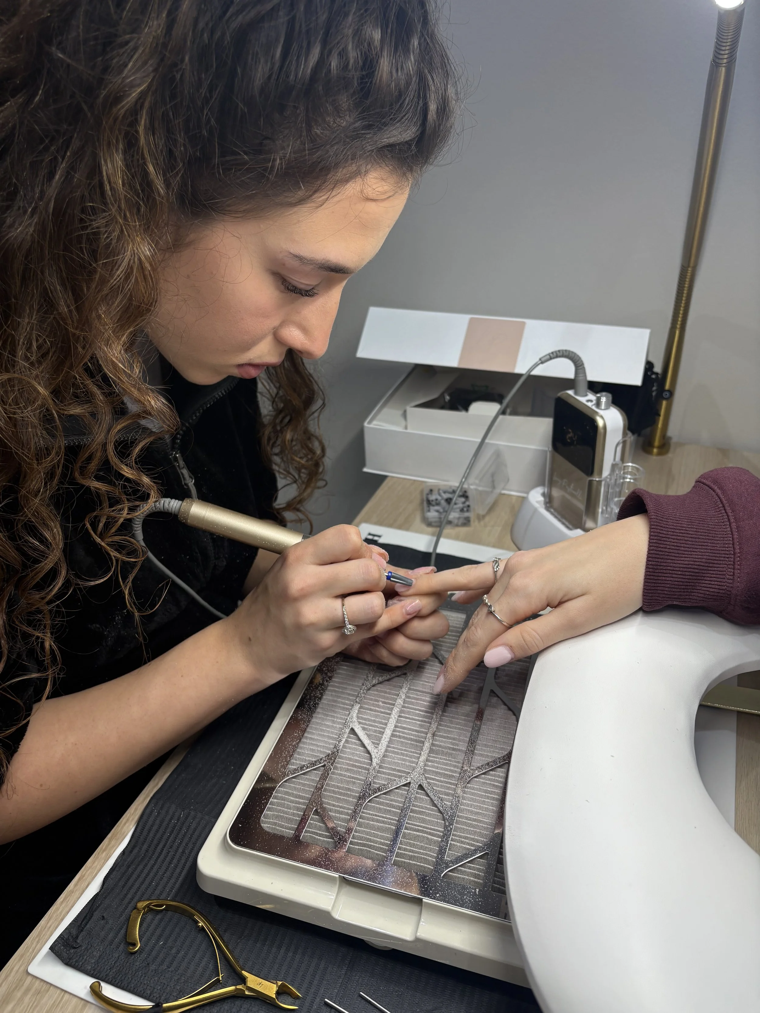 A woman is applying nail polish or a nail design to another person's fingernail in a nail salon.