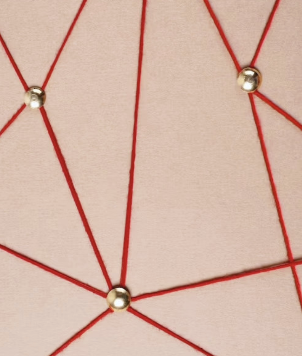 Close-up of a decorative pinboard with red string arranged in geometric patterns, secured by gold-colored push pins.