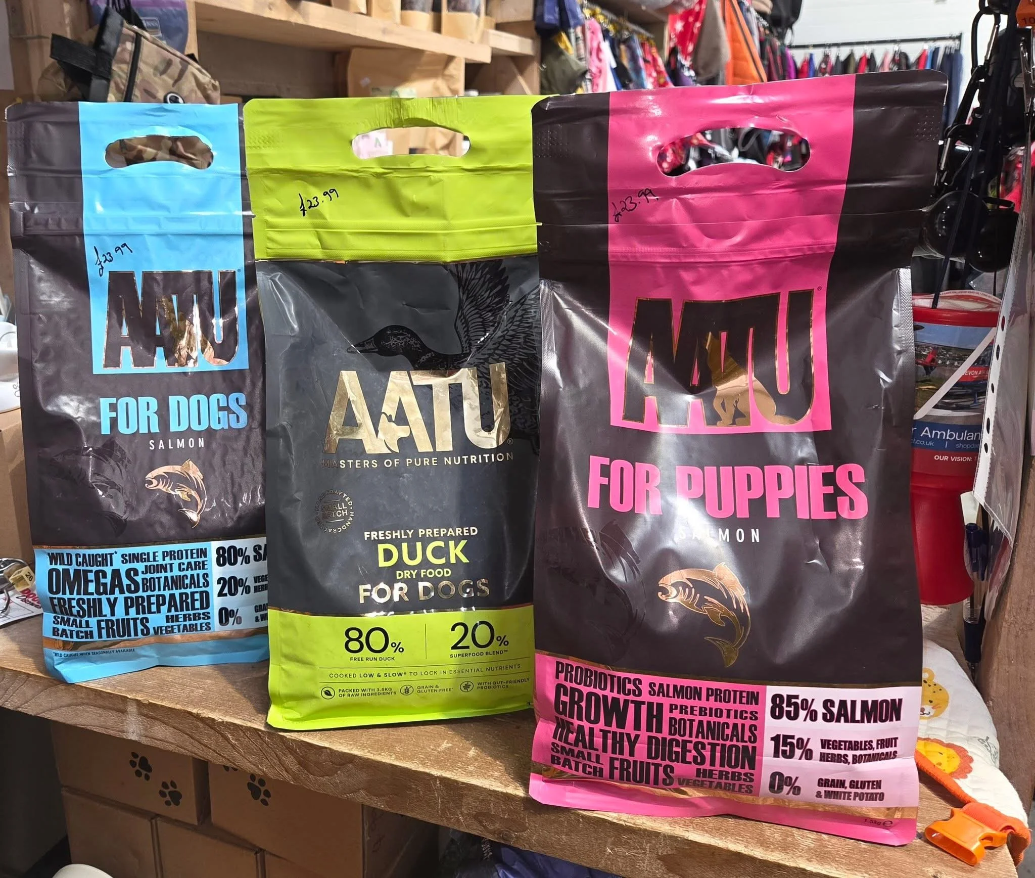 Three bags of dog and puppy food on a wooden surface. The bags are labeled for dogs and puppies, with colorful designs and nutritional information.