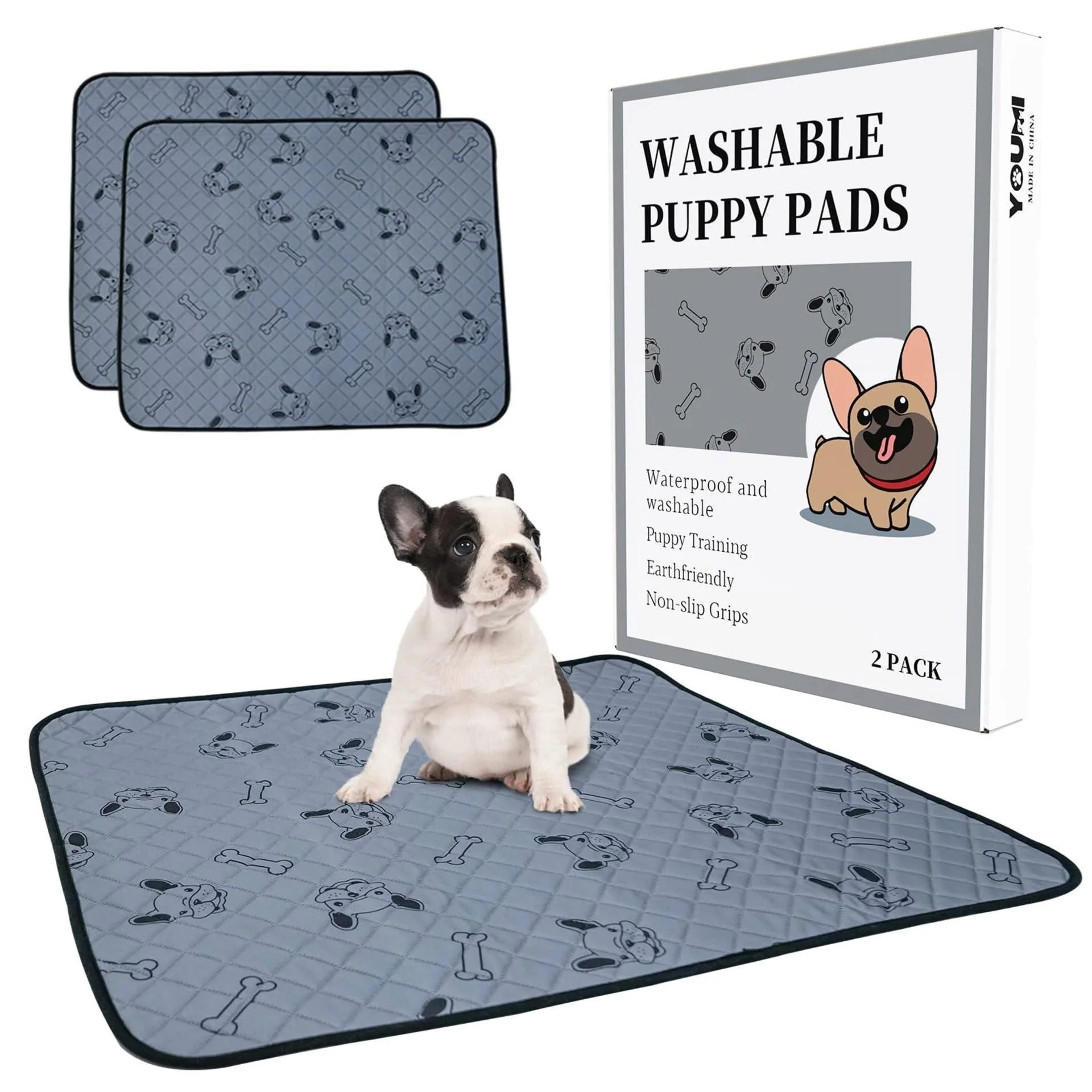 A small puppy sitting on a washable puppy pad with a matching pad lying next to it, and a box of washable puppy pads with an illustration of a French Bulldog on the packaging.