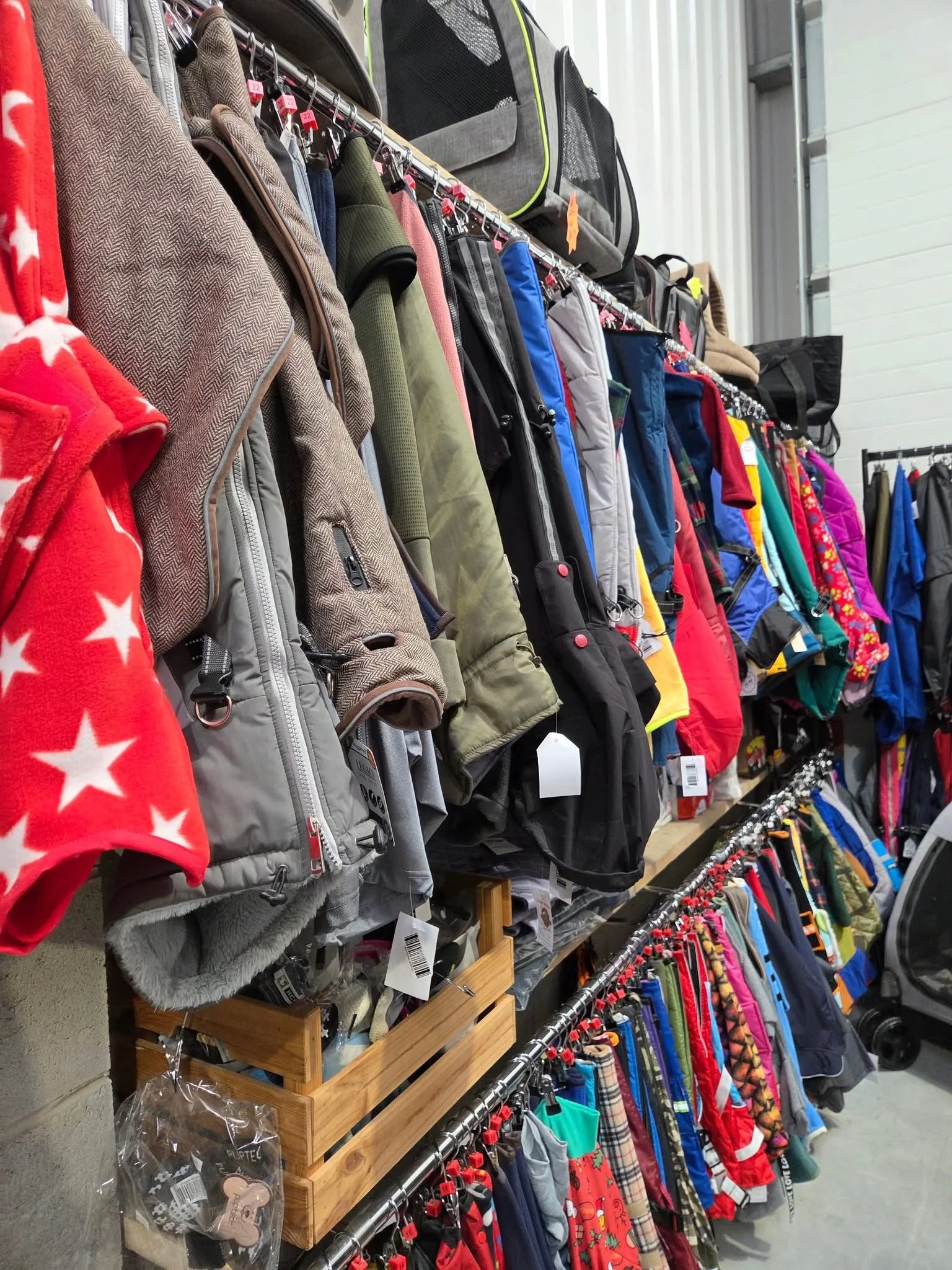 Clothing store display with various jackets, coats, and outerwear hanging on racks, including holiday-themed pajamas and accessories.