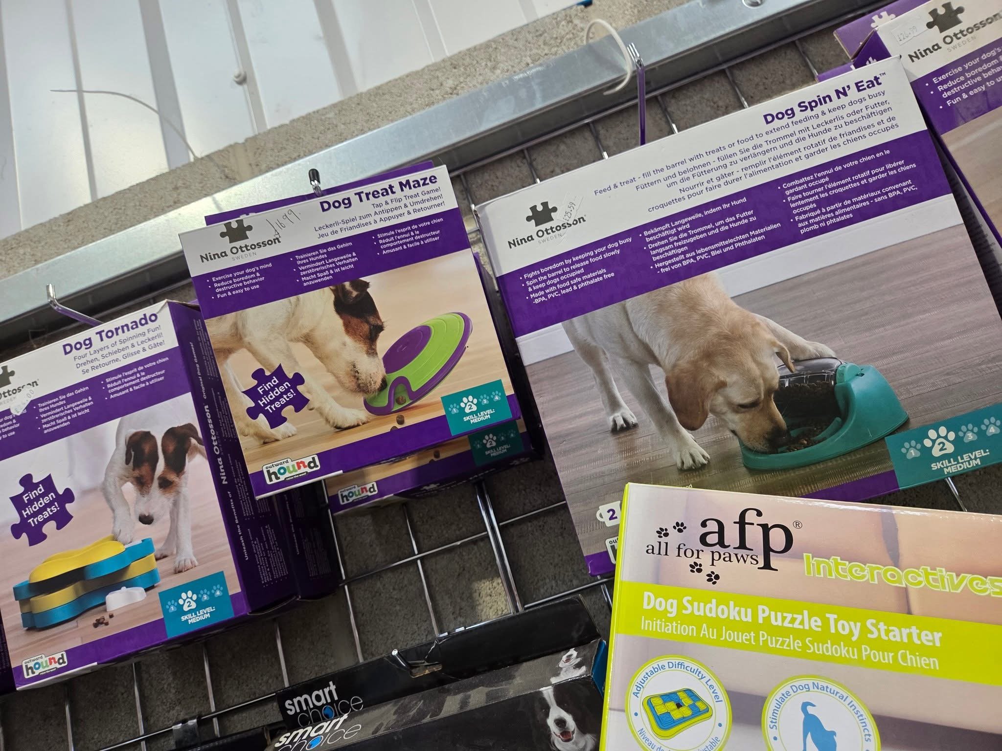 Dog puzzle toys and treat maze for dogs on display, with images of dogs eating from the toys on the packaging. The packaging features a yellow and white color scheme with purple accents.