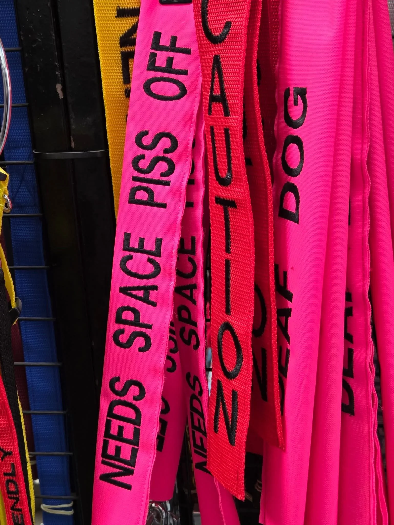Pink and red fabric lanyards with black text, hanging on a metal display rack.