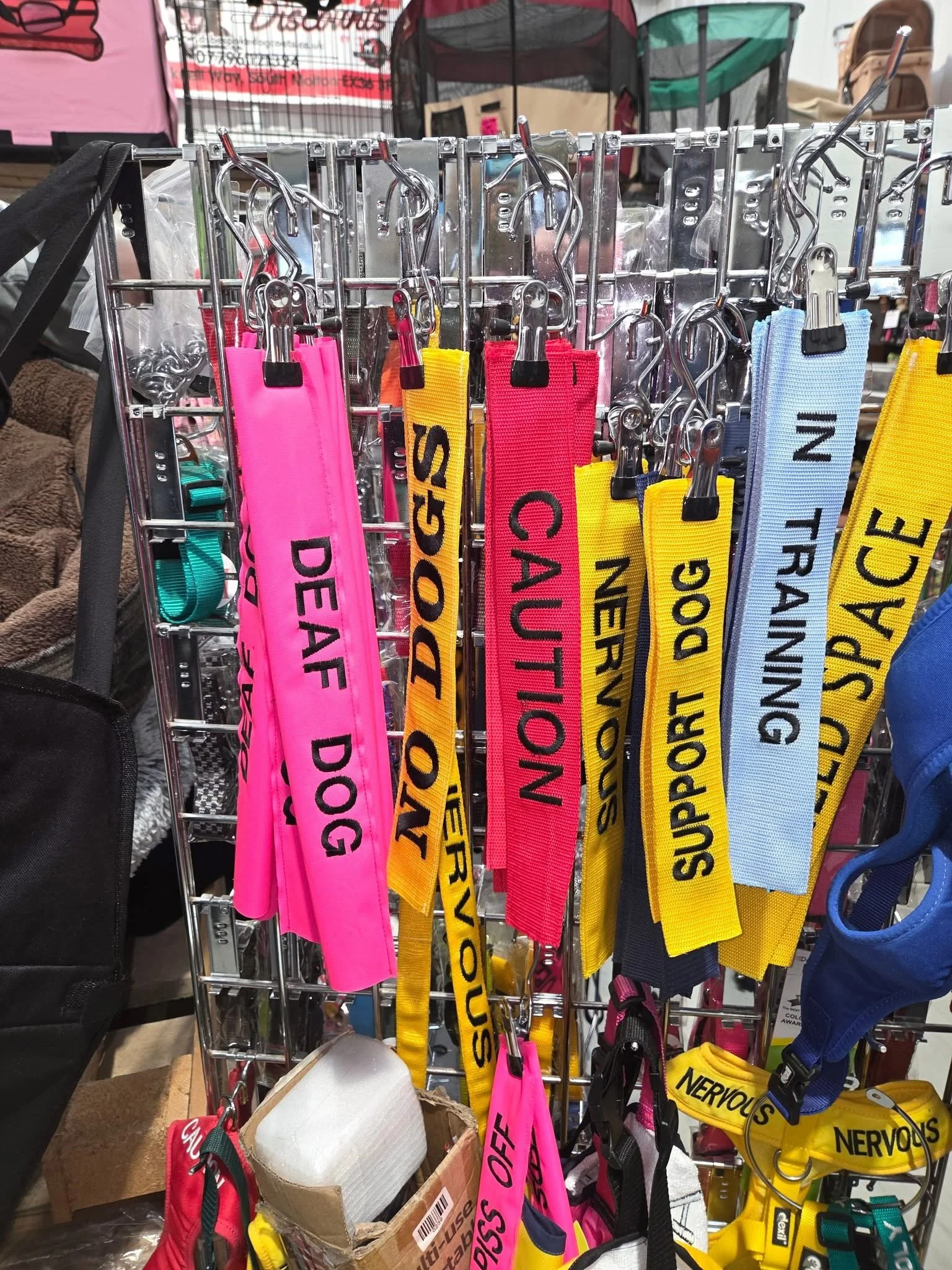 Colorful pet leashes hanging on a display rack, with labels such as 'Deaf Dog,' 'Sound,' 'Caution,' 'Nervous,' 'Support Dog,' 'Training,' and 'Space.'
