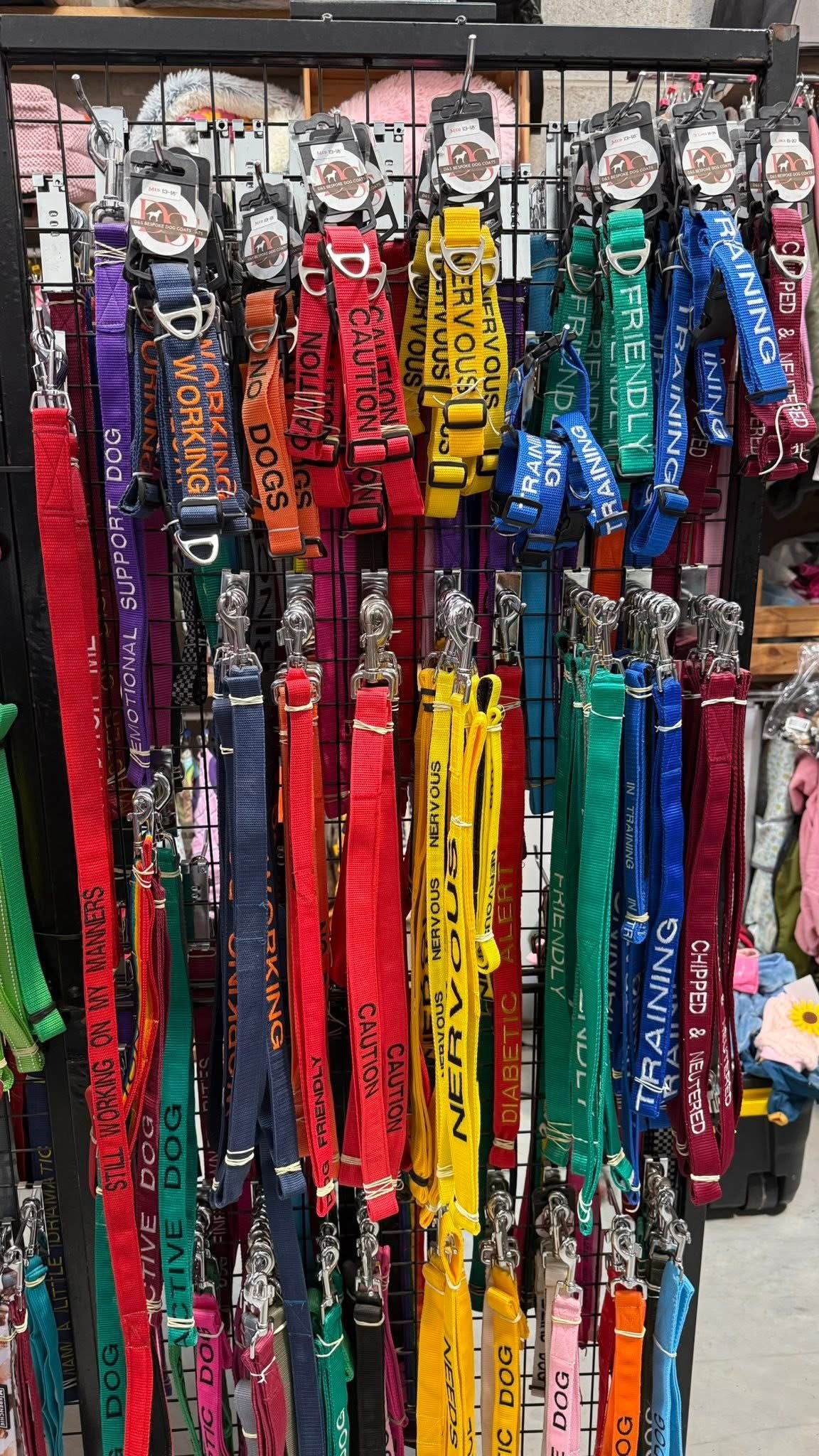 Colorful dog collars and leashes hanging on display, with various messages like 'Support Dog,' 'Training,' and 'Caution' printed on them.
