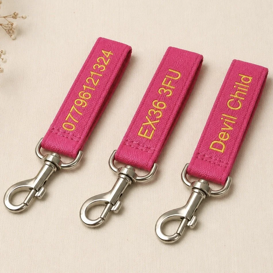 Three pink fabric keychains with yellow embroidered text and metal clips, each labeled with different emergency contact or health information.