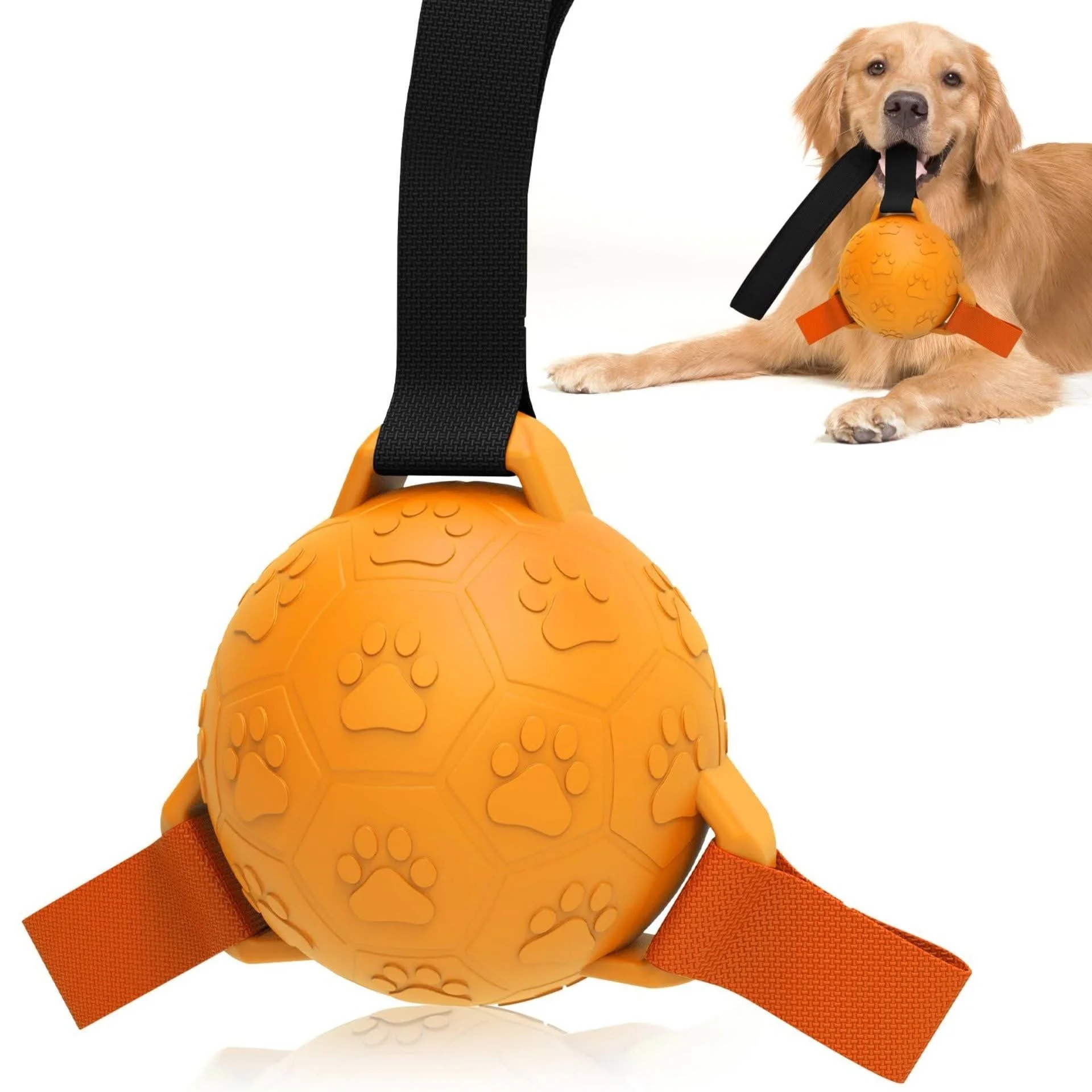 A close-up of an orange rubber dog toy with paw print and hexagon patterns, attached to a black strap with orange fabric loops, with a golden retriever lying down in the background chewing on a similar toy.