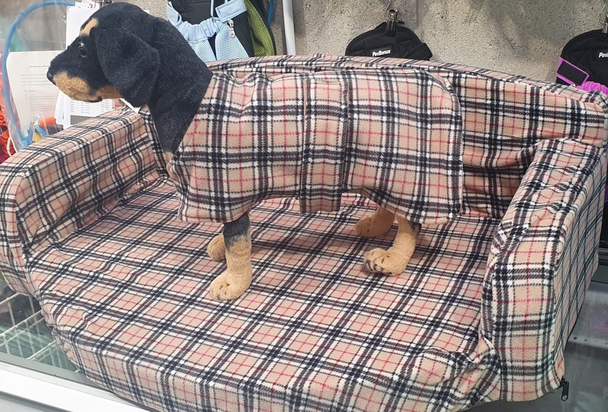 A dog dressed in a plaid coat sitting on a couch with a matching blanket covering its body.