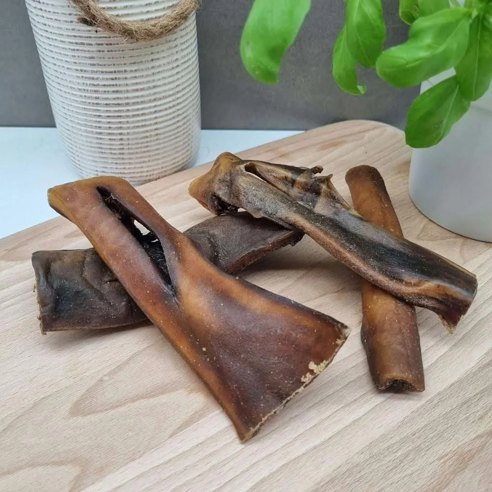 A wooden board with several dried fish skins, some with visible openings, placed near a potted plant and a white container in the background.