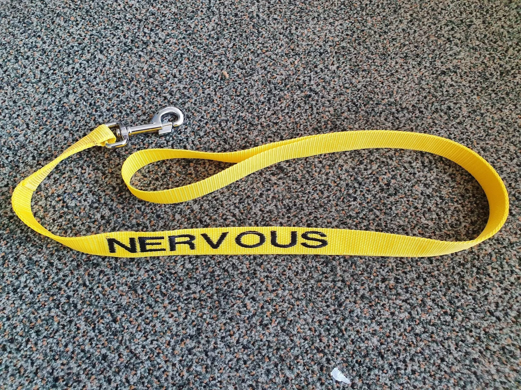 Yellow lanyard with the word 'Nervous' written on it, lying on a gray carpeted floor.