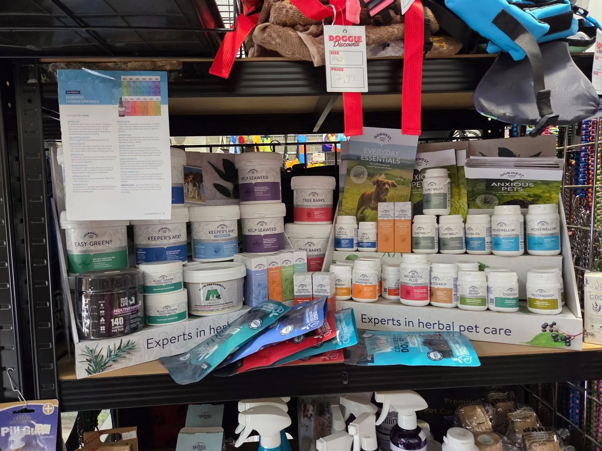 Display of herbal pet care products including supplements, powders, and treats at a store shelf, with labels indicating brands and product types.