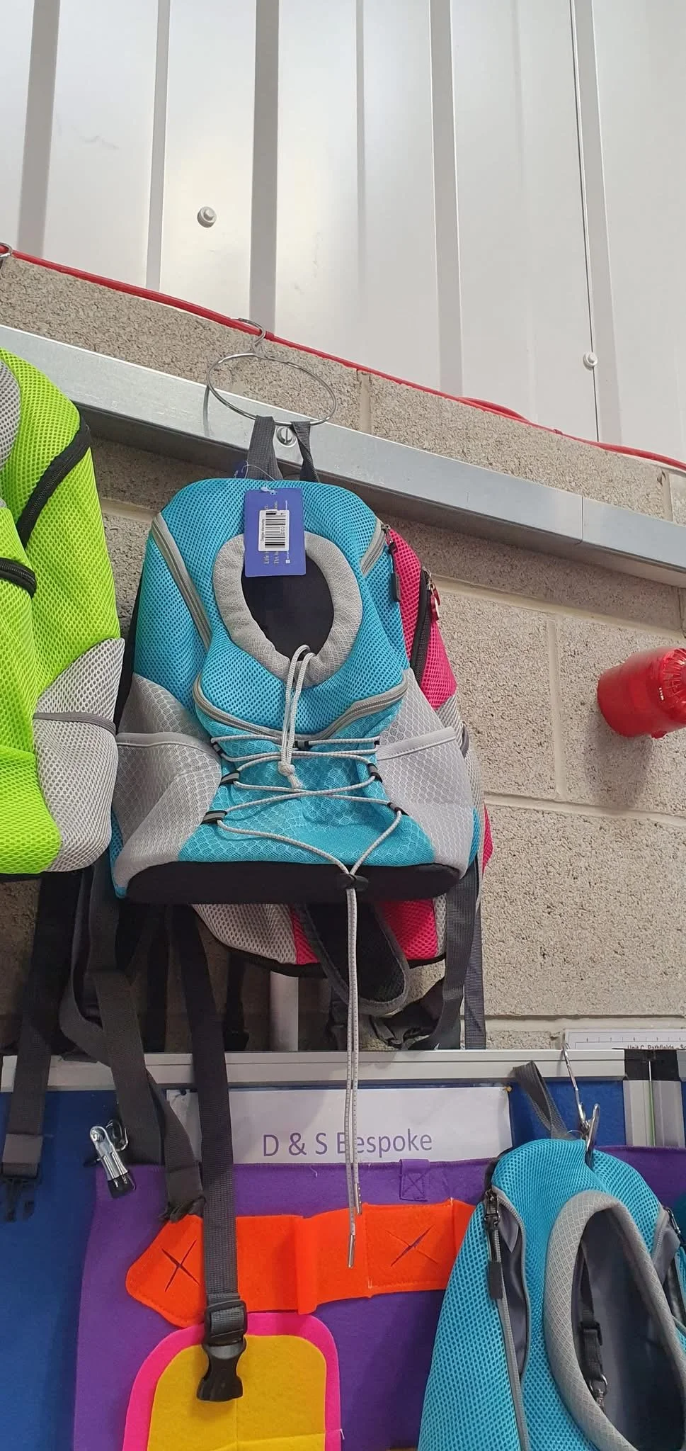 Colorful backpacks hanging on display hooks against a brick wall at a store.