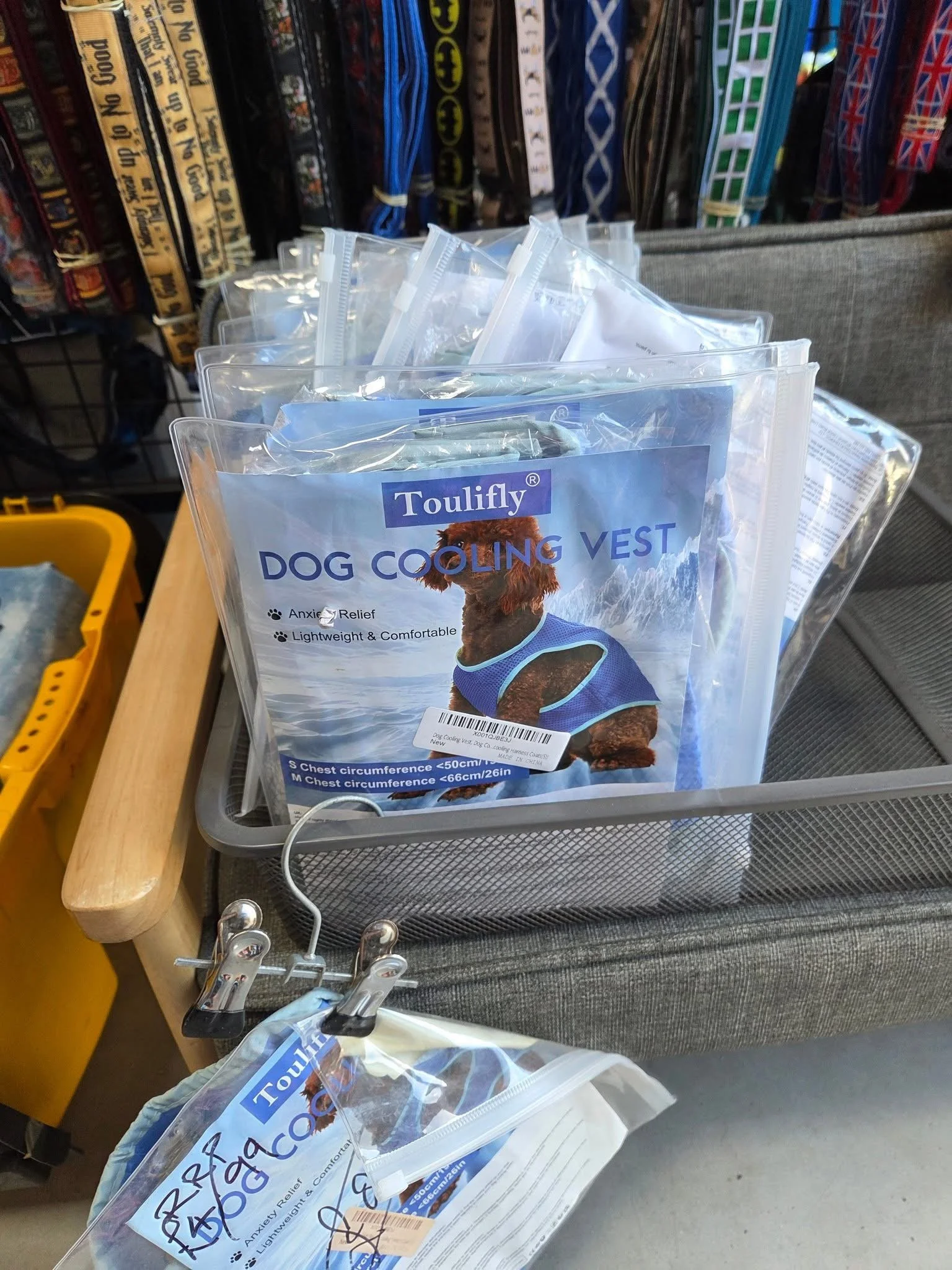 A display of dog cooling vests in plastic packaging on a store shelf, with a background of books and a gray fabric-covered display stand.
