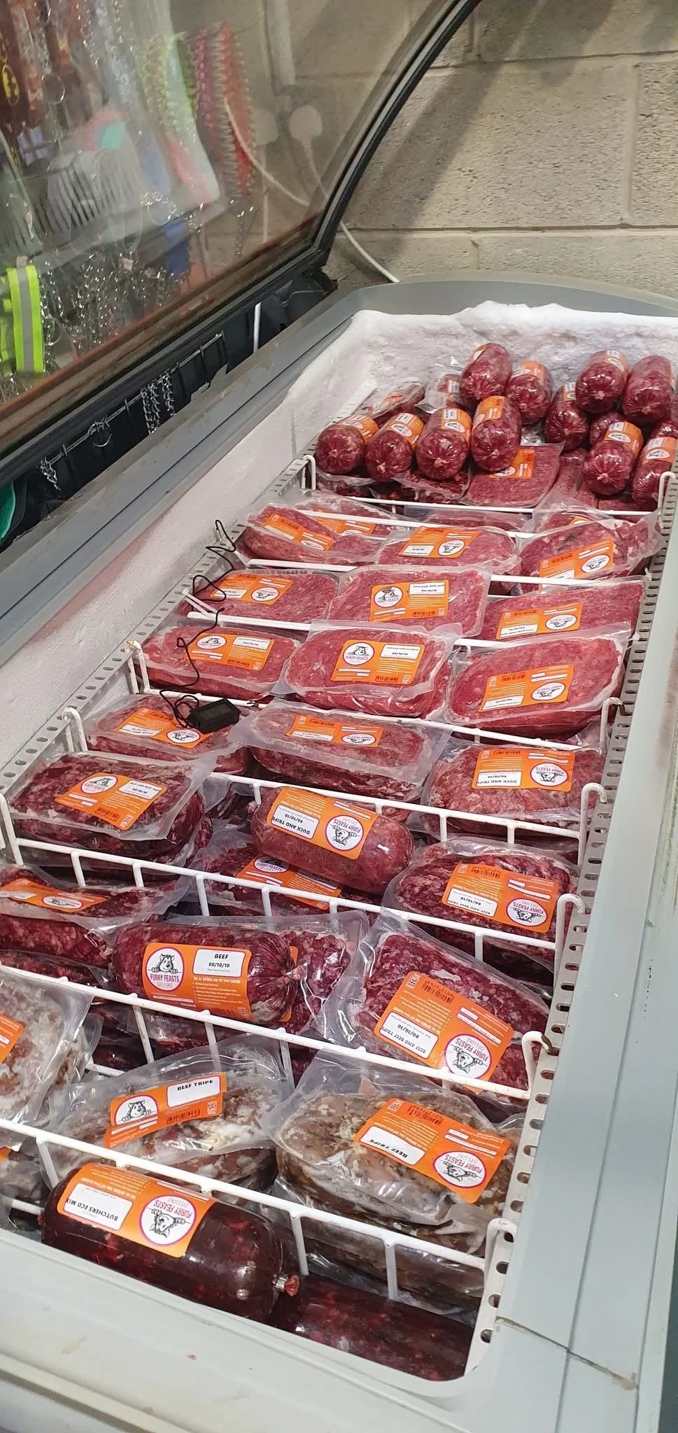 Frozen meat cuts and sausages inside a refrigerated freezer, with orange and white labels.