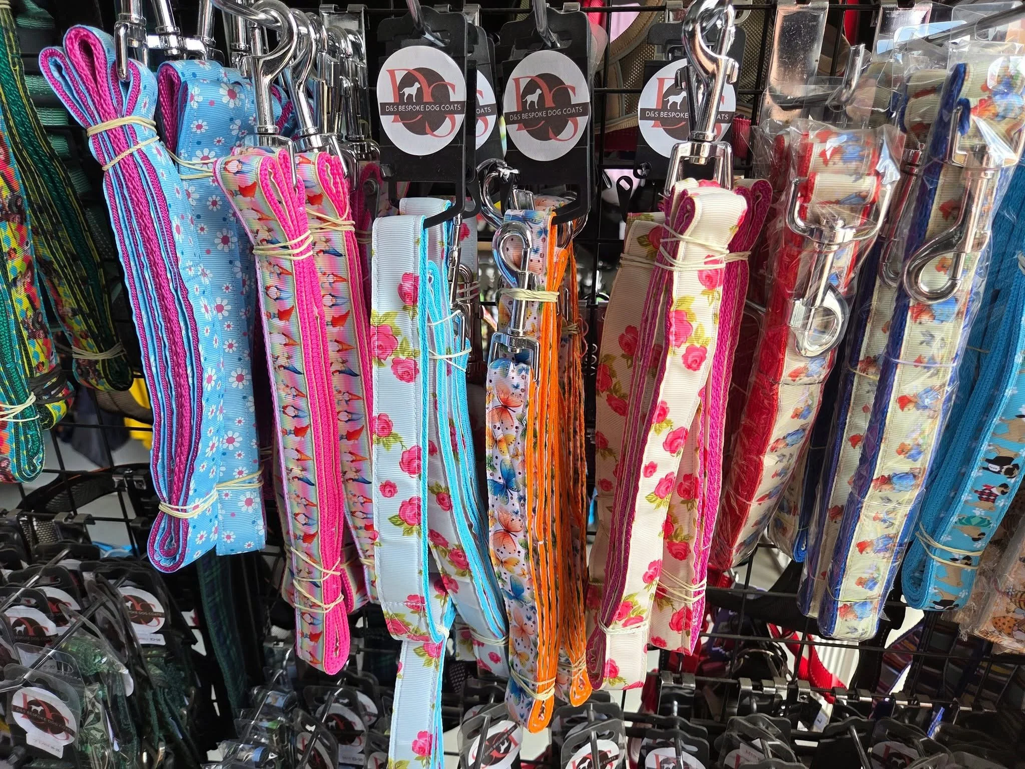 Colorful dog leashes with various floral and striped patterns hanging on display hooks in a pet store.
