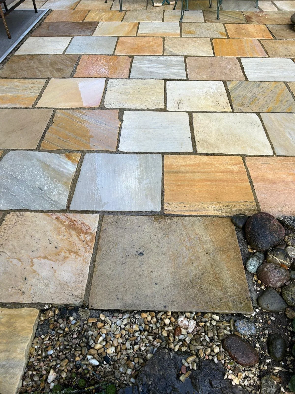 Wunderschöne bunte Natursteinpflasterung auf einem Gehweg, mit kleinen Kieselsteinen und einigen größeren Steinen in der Ecke.