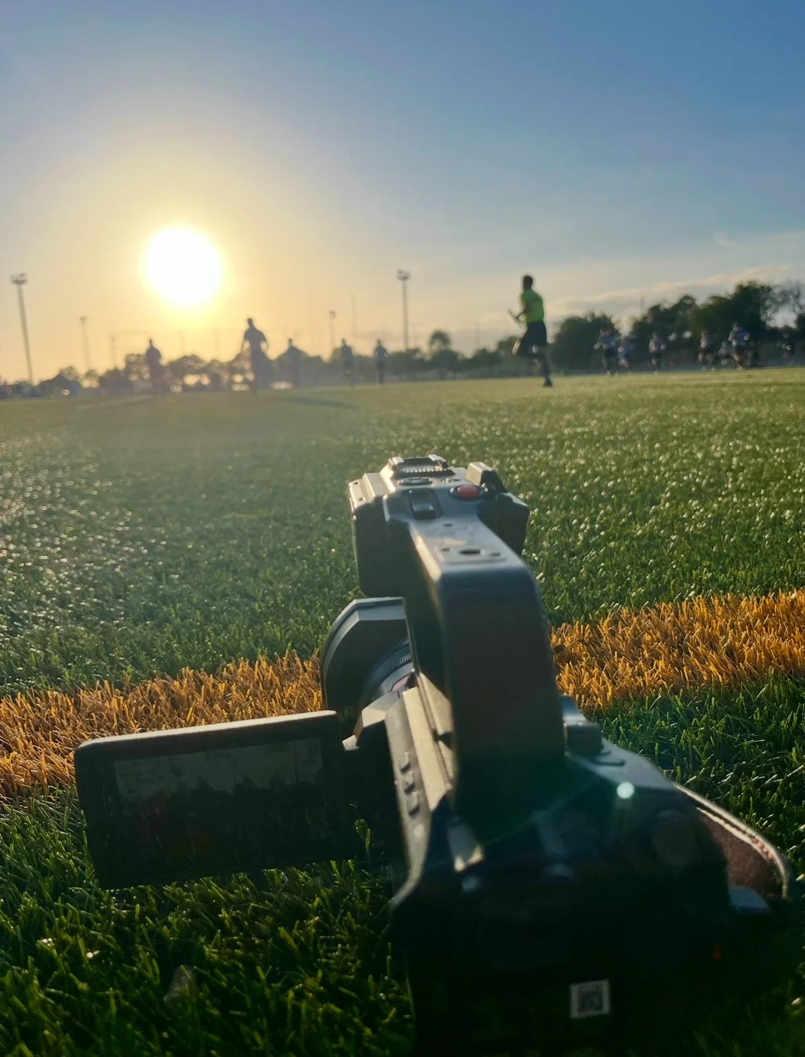 A football field during sunset with players and coaches in the distance, and a laser tag gun in the foreground.
