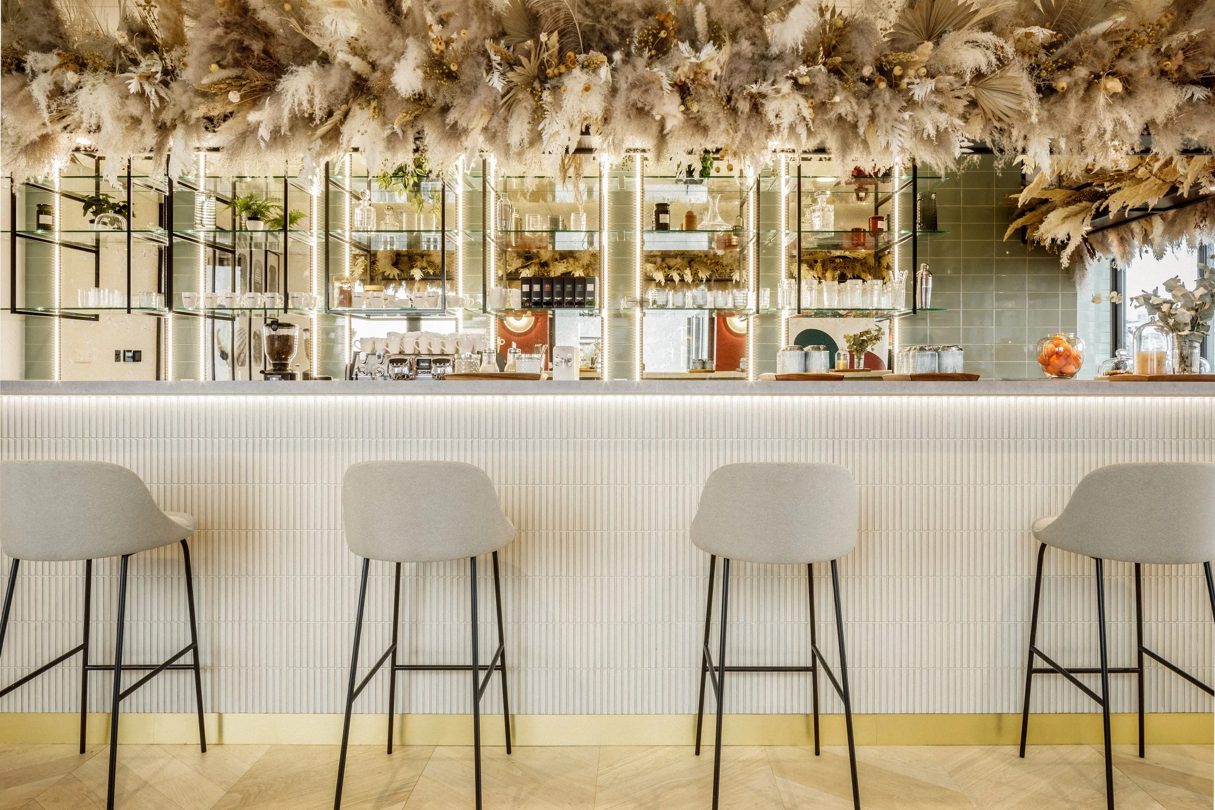 Intérieur d'un espace de bureau moderne et lumineux avec un coin salon pink et des coussins, séparé par des étagères en noir, avec des lampes en fil de cuivre suspendues au plafond.