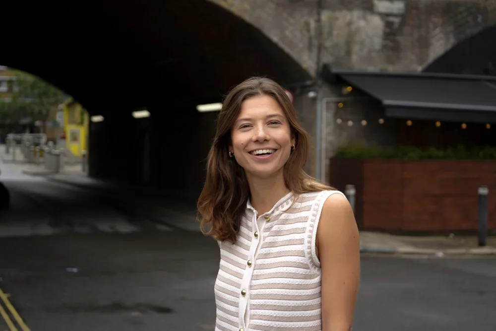 Young woman with brown hair smiling outdoors under an archway