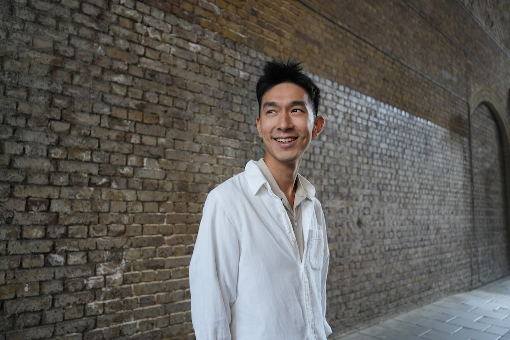 Smiling man in white shirt standing next to a brick wall.
