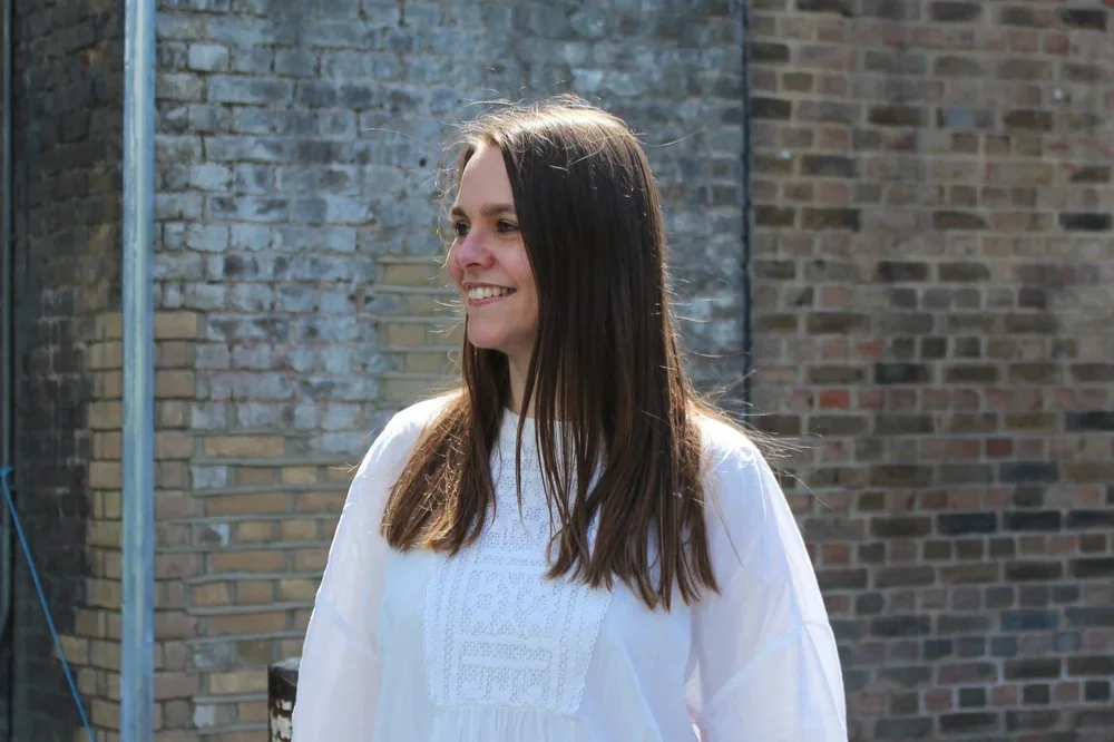 A woman with long dark hair smiling outdoors in front of a brick wall.