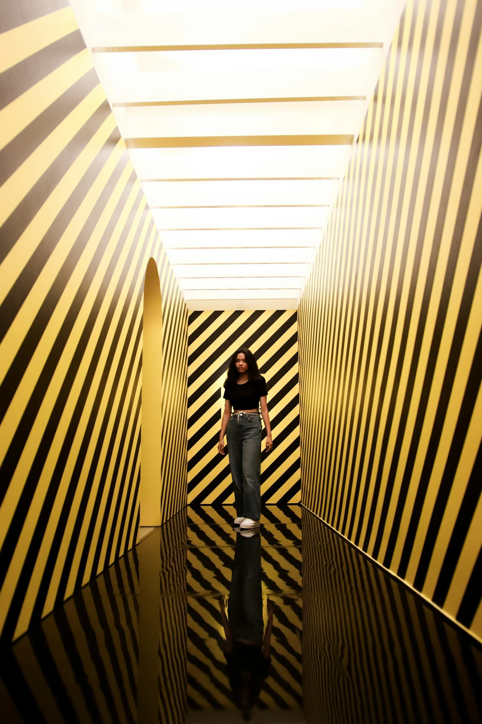 A woman walking through a corridor with yellow and black striped walls and a black and yellow patterned floor.