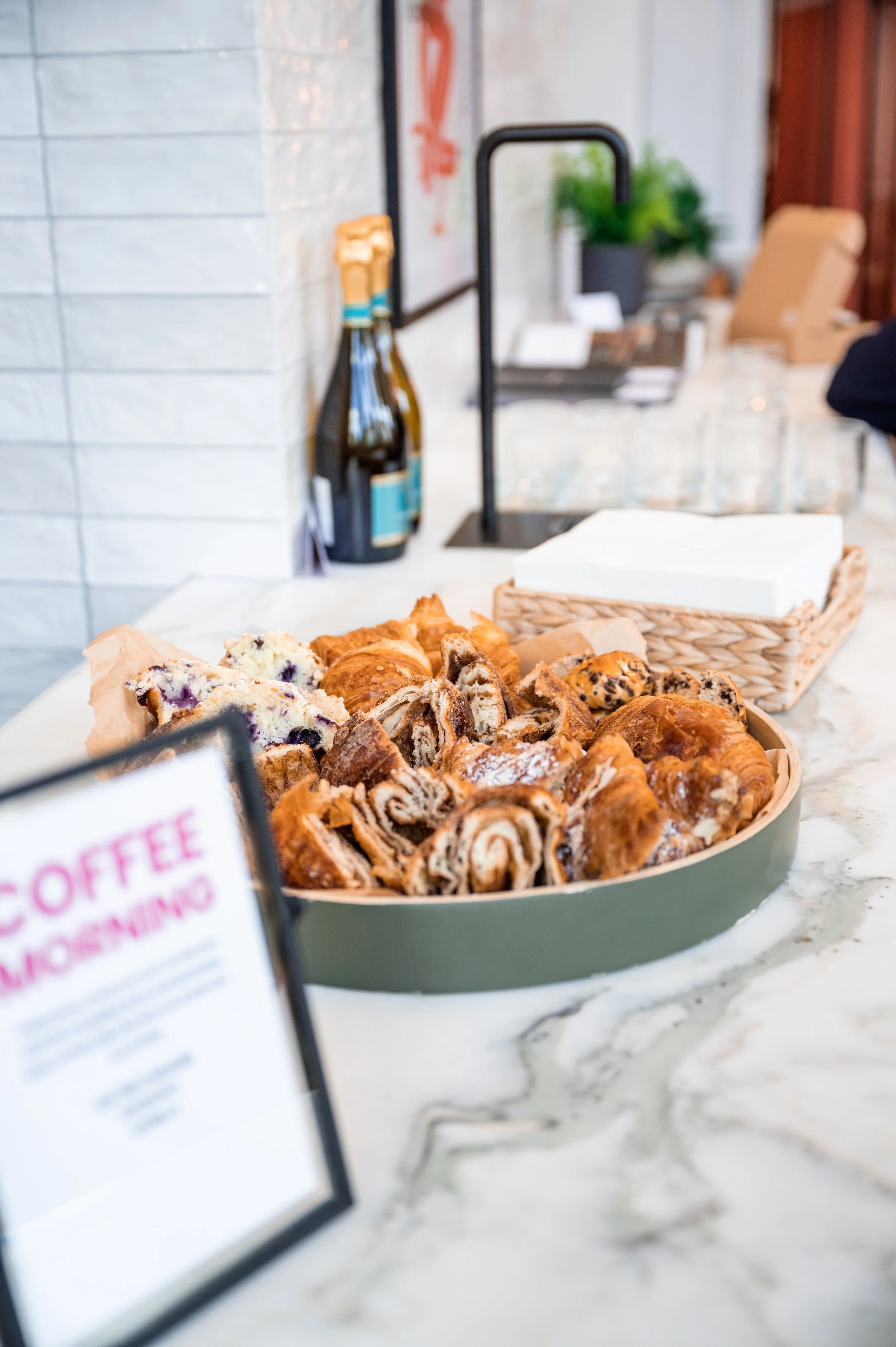 Assorted pastries including croissants and cinnamon rolls on a marble countertop with a blurred sign in the foreground.